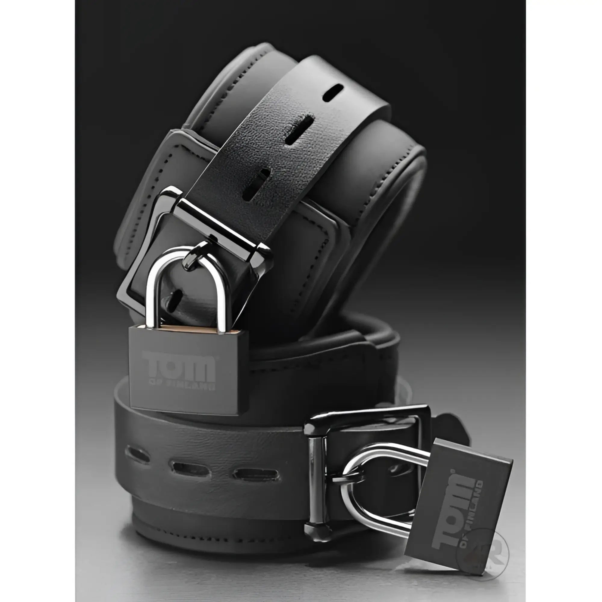 Tom of Finland black neoprene wrist cuffs with adjustable straps, silver buckles, and branded silver padlocks.