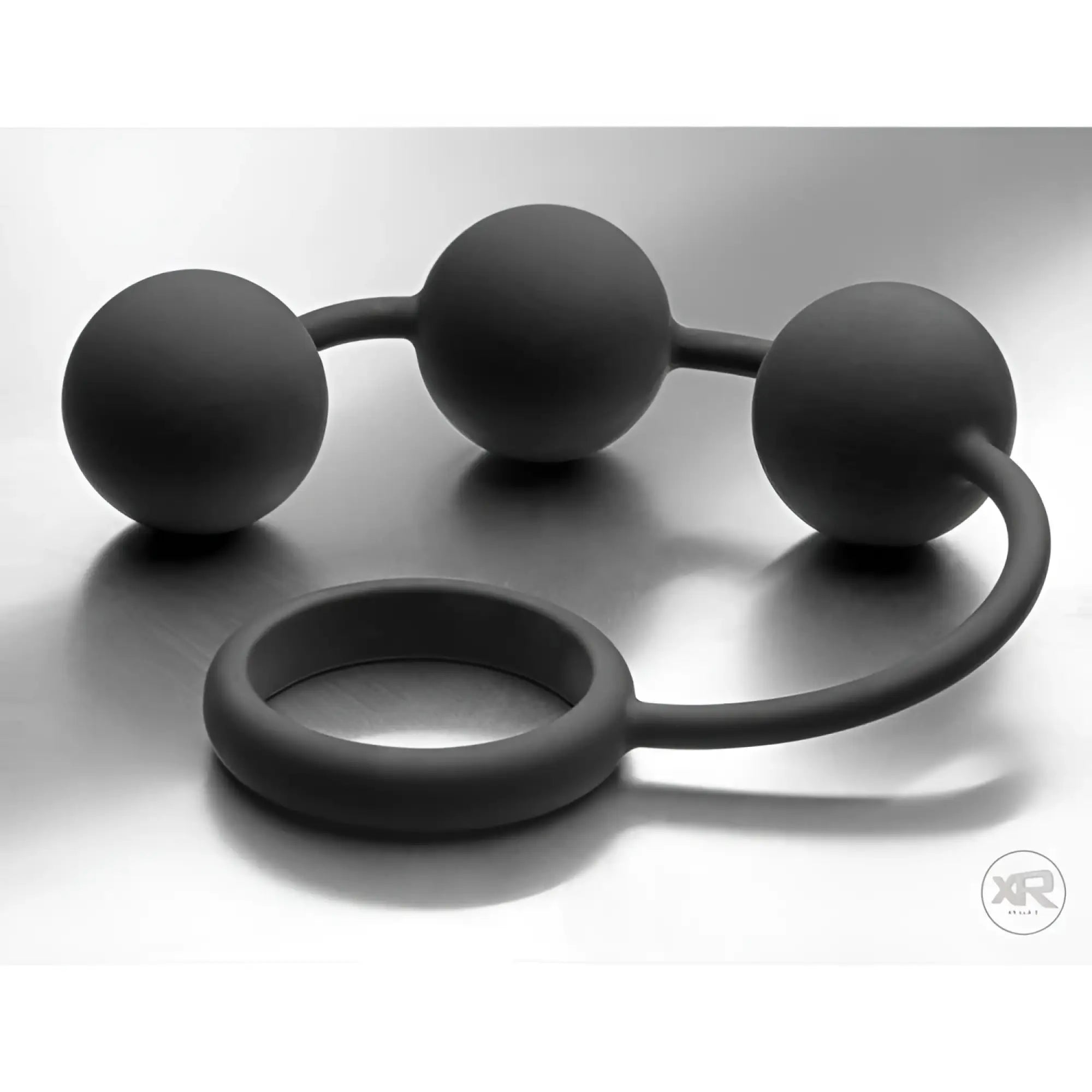 Tom of Finland matte black silicone cock ring with three attached weighted anal balls on a silver background.