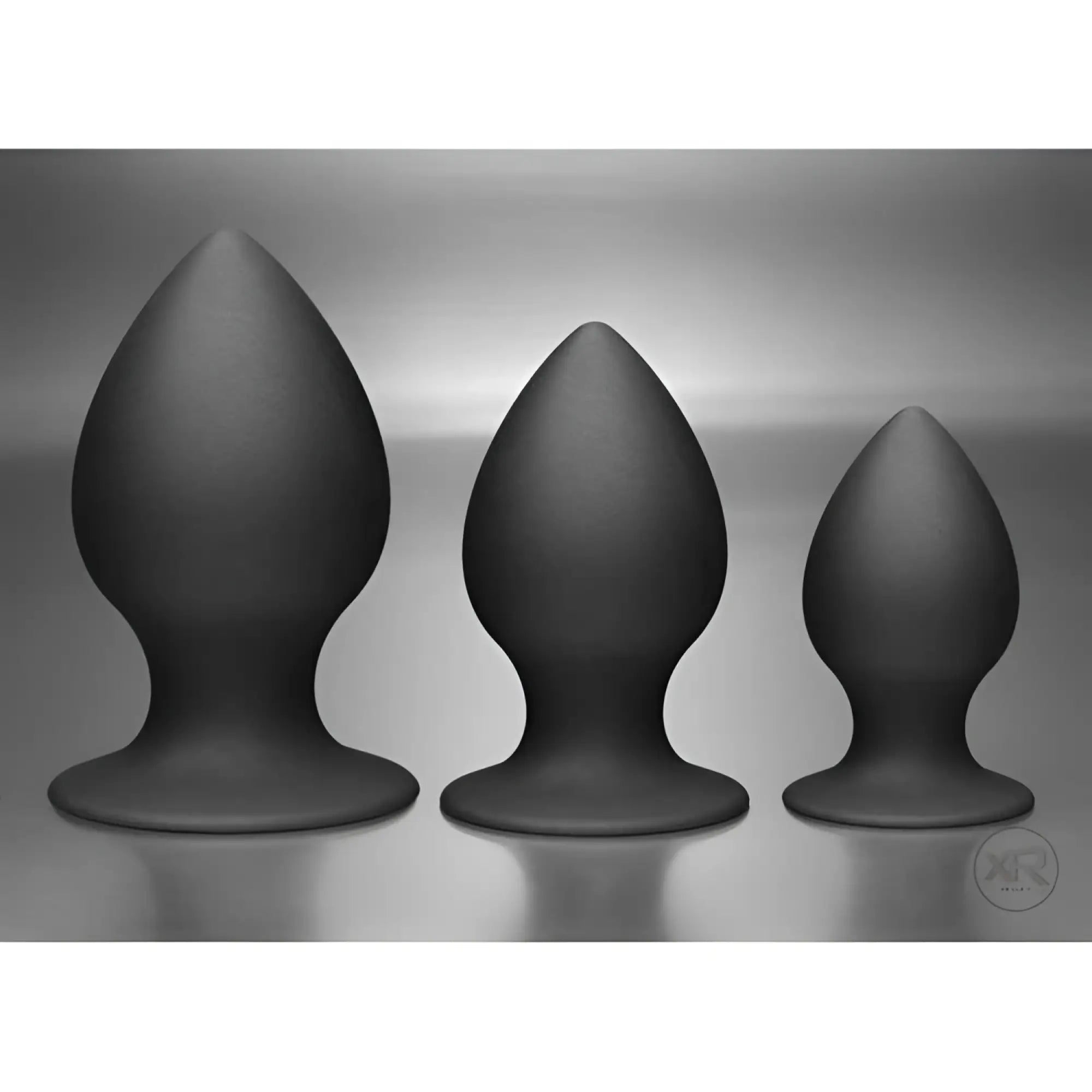 Three matte black Tom of Finland silicone anal plugs of varying sizes, standing upright against a grey background.