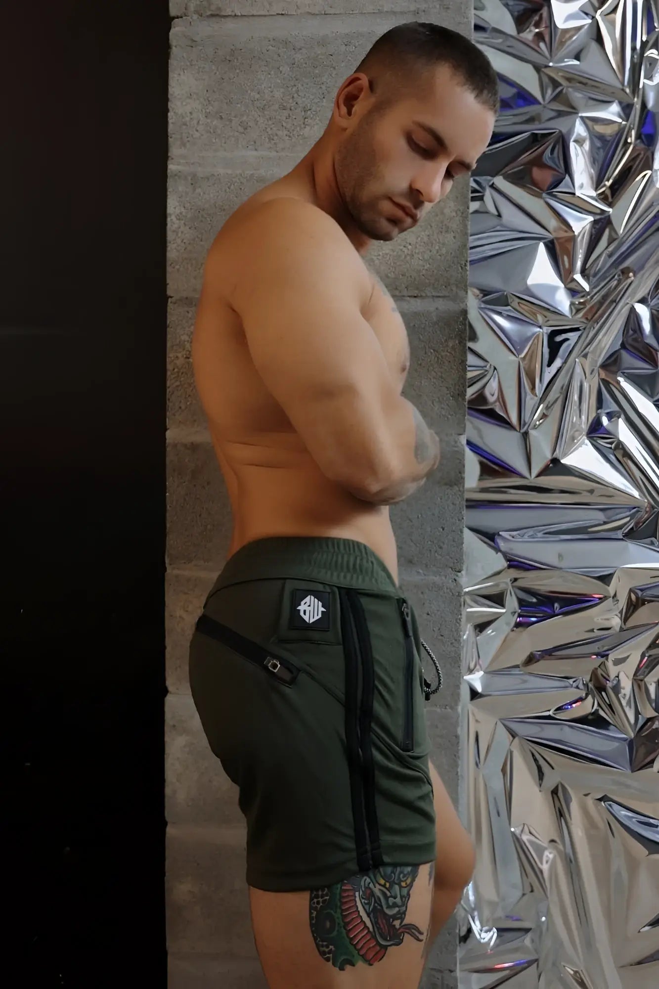 Dark green trade trainer shorts with black zipper accents and a small logo patch on the back waistband shown from behind