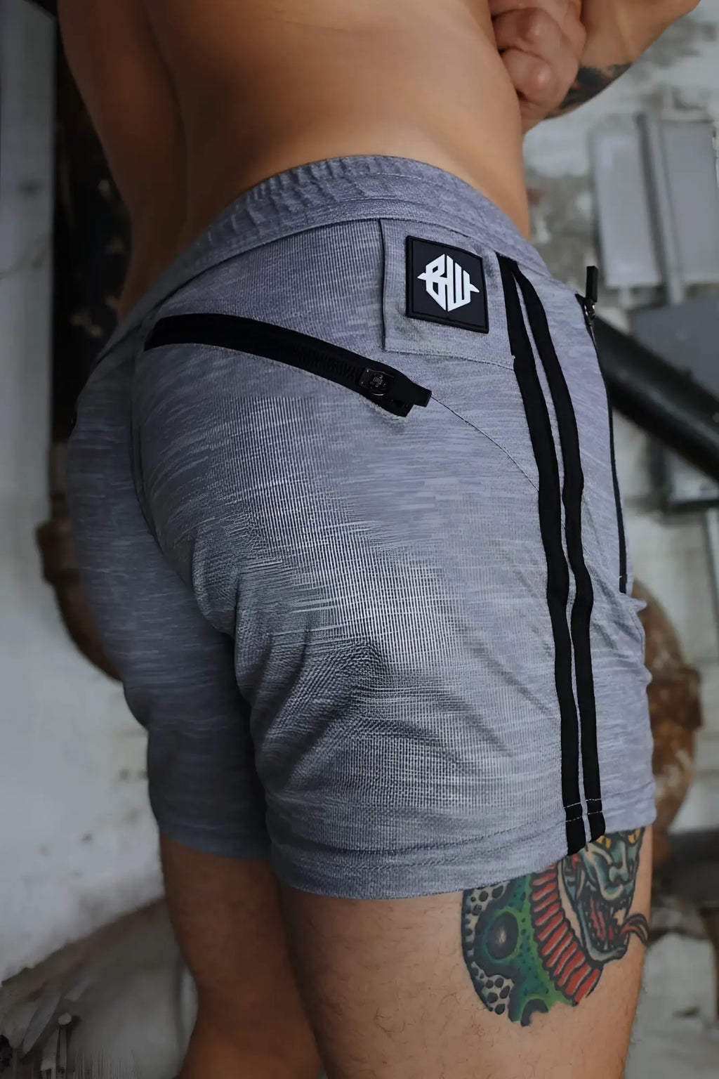 Back view of gray heathered trade trainer shorts with black side stripes and branded patch on waistband