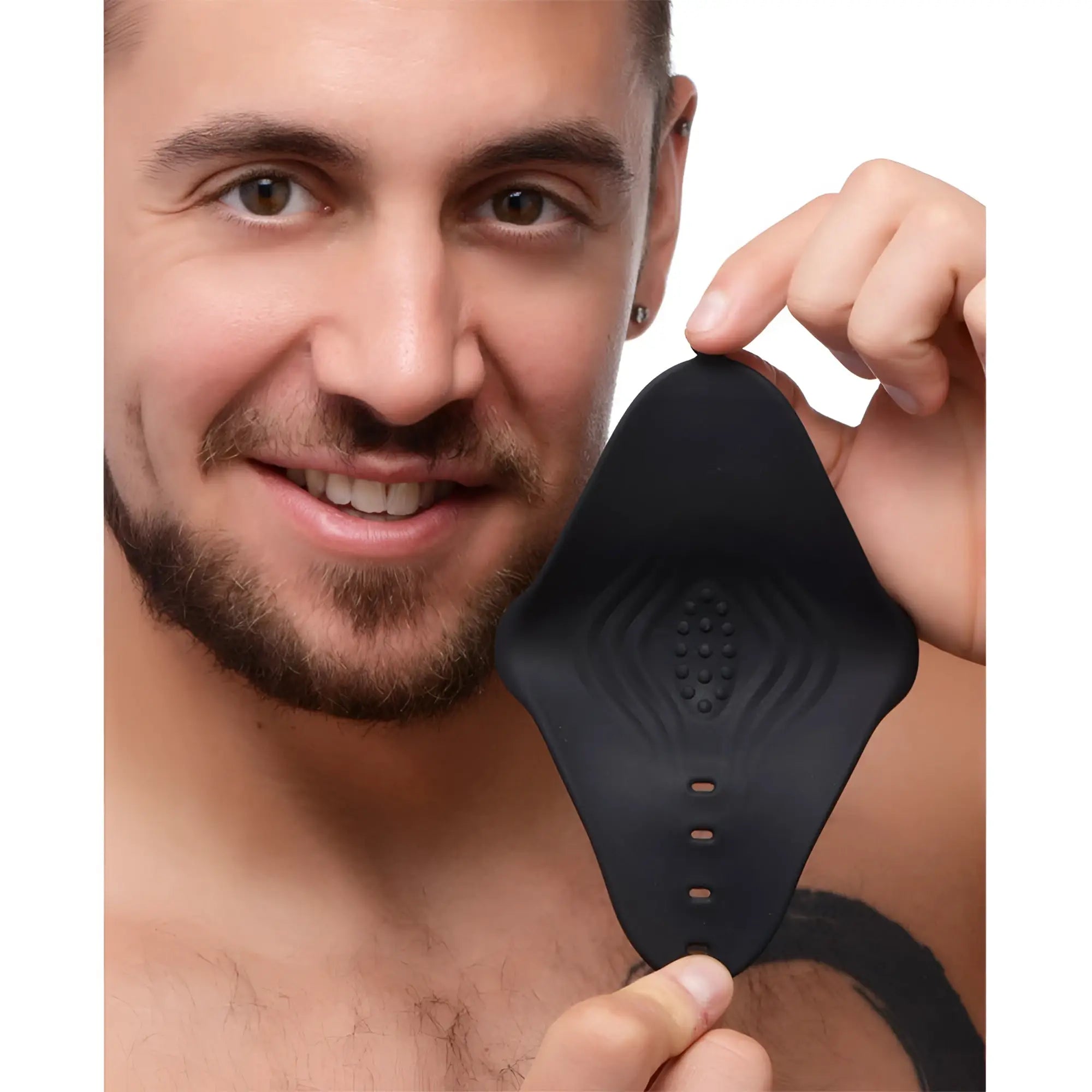 A man holds a black, diamond-shaped Trinity Men 10X silicone pleasure sleeve with a textured, ribbed interior.