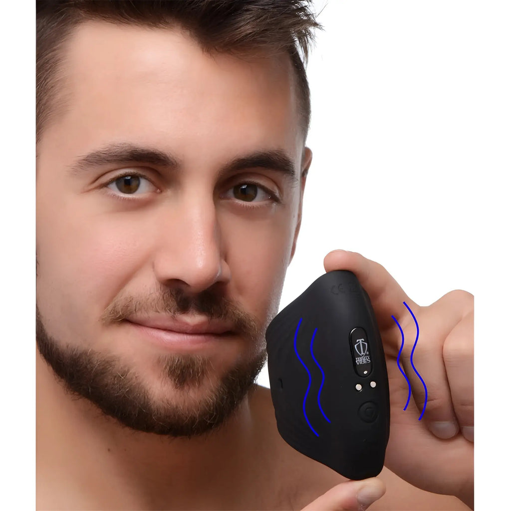 A smiling man holds a black Trinity 10X Pleasure Stroke vibrating silicone penis sleeve with blue graphic waves.