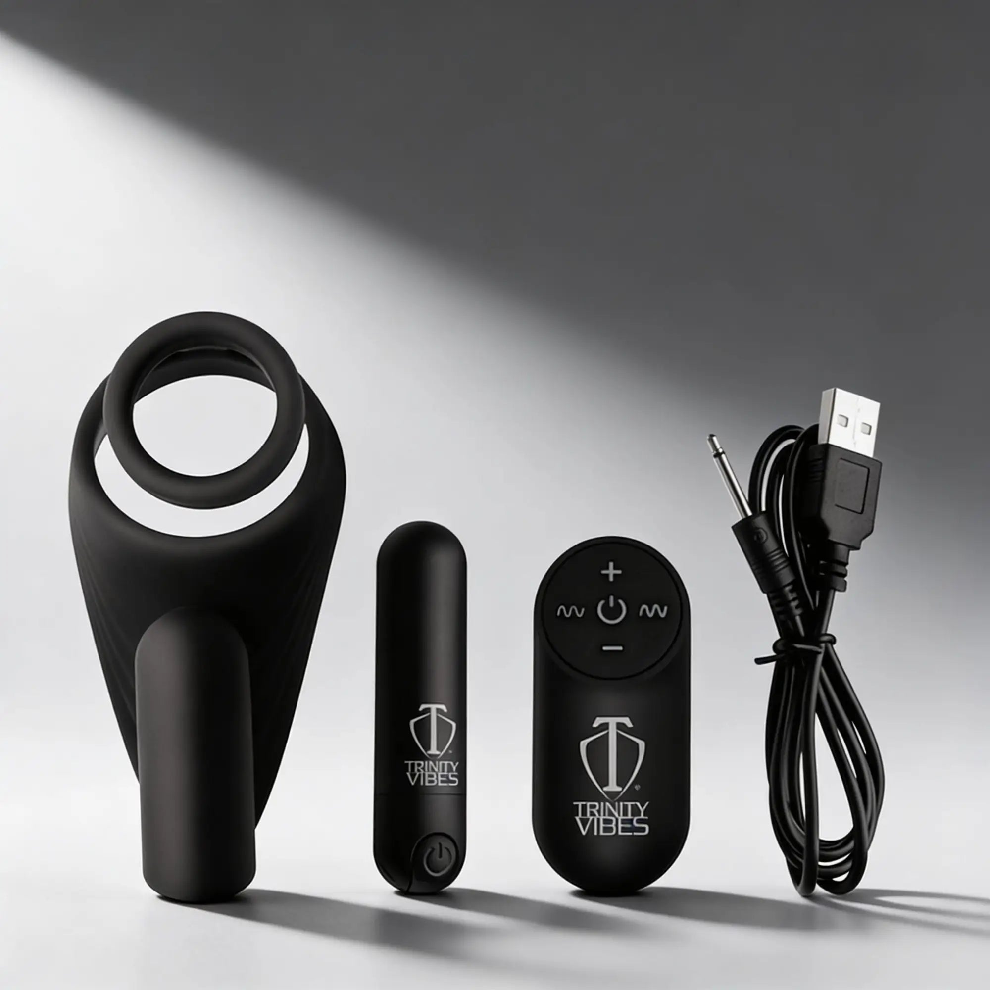 Trinity Men 7X black silicone c-ring, vibrating bullet, remote control, and USB charging cable on a gray background.