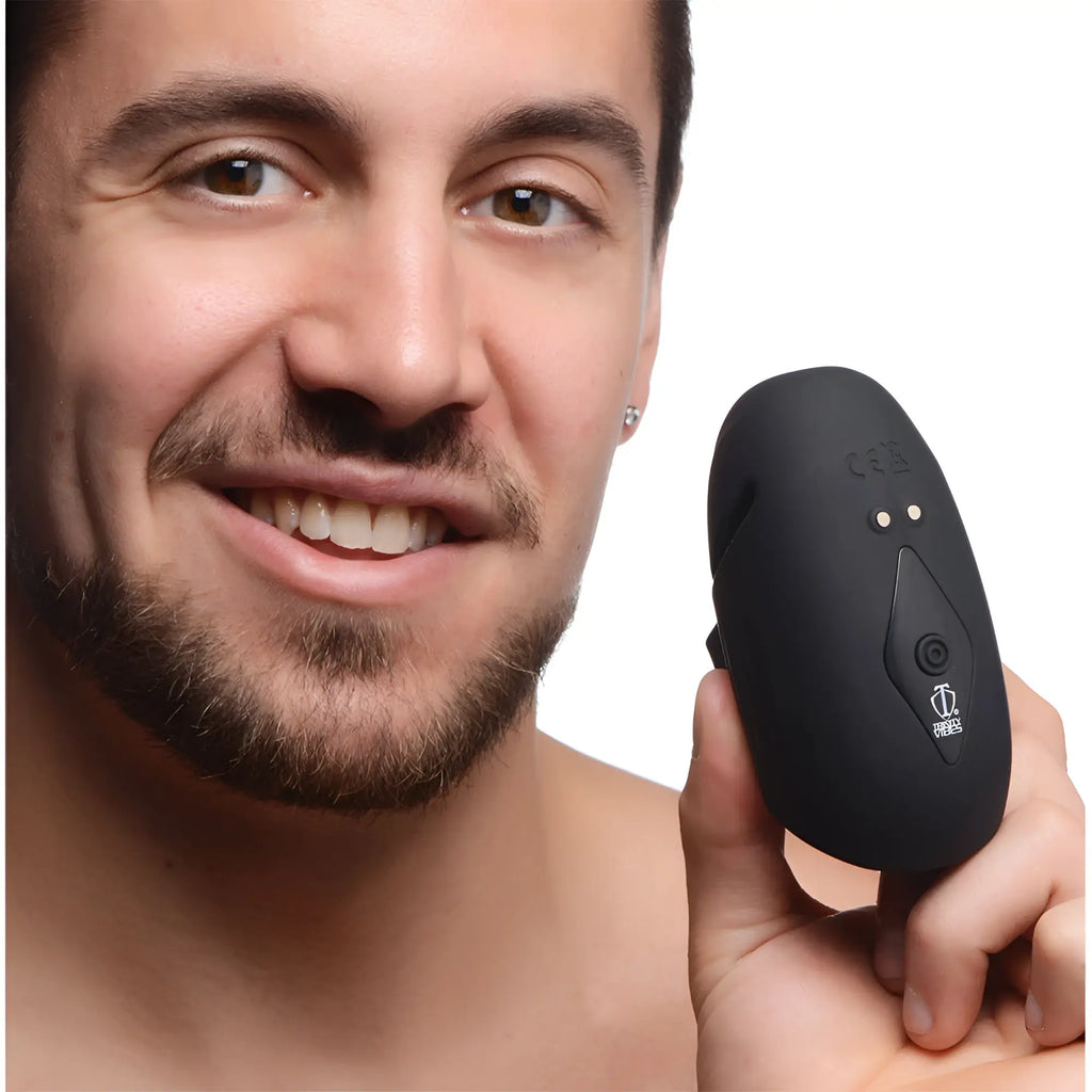 A smiling man holds a black, egg-shaped Trinity Men 8X silicone penis head stimulator.