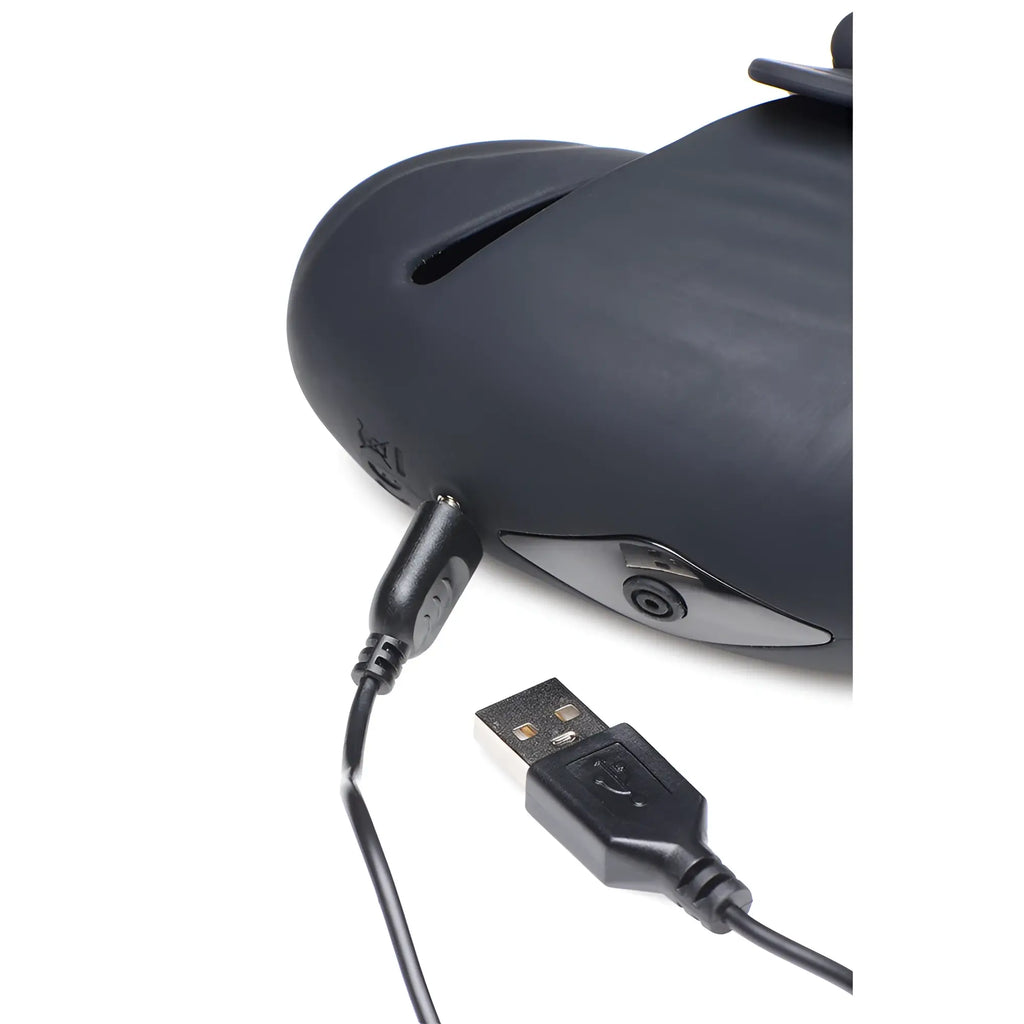 Trinity Men 8X black silicone head stimulator shown with a charging cable plugged into the device port.