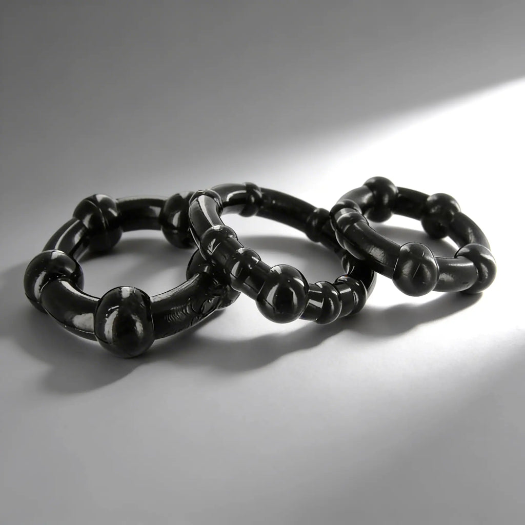 Three black Trinity Men Erection Enhancement rings with beaded, textured designs arranged on a light gray surface.