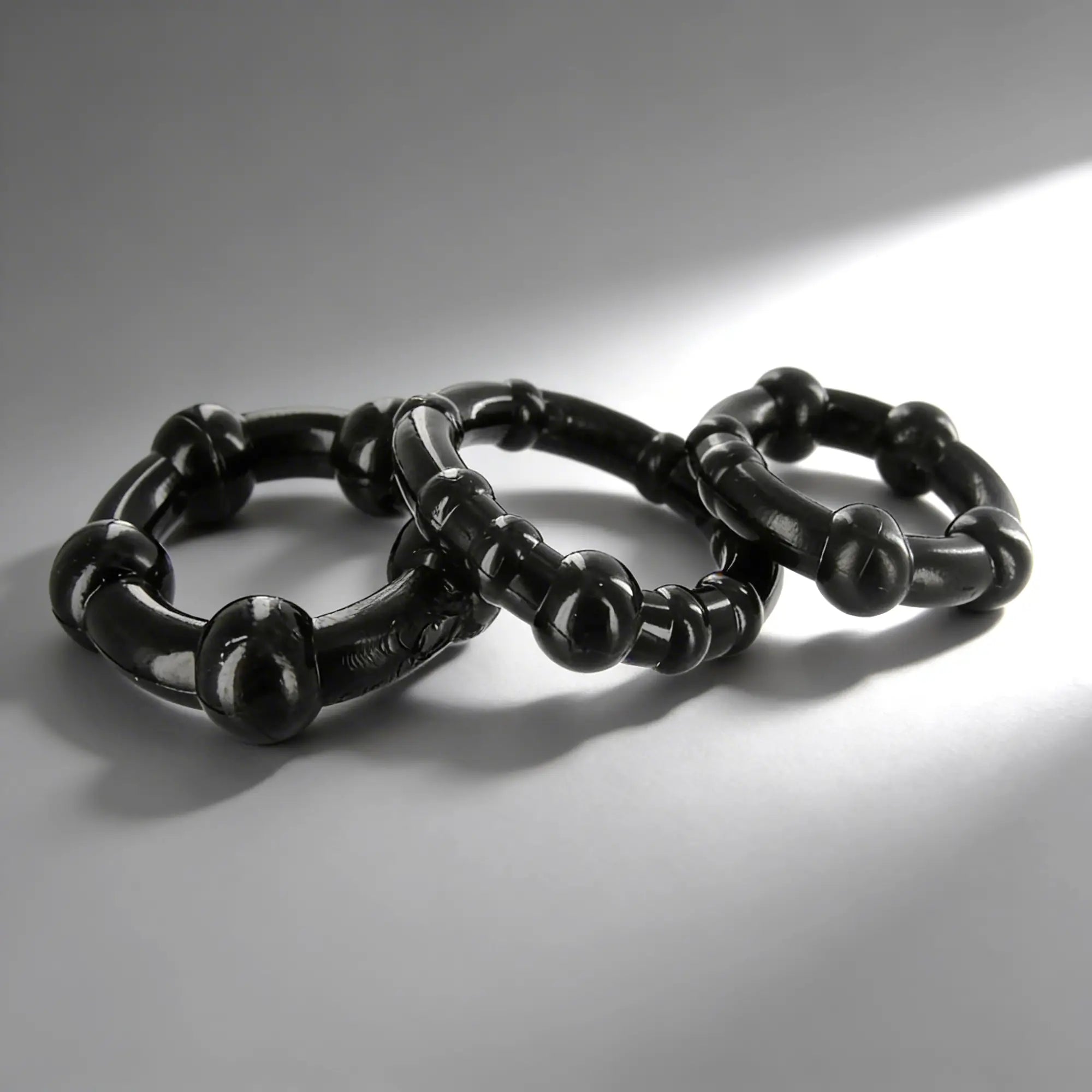 Three black Trinity Men Erection Enhancement rings with beaded, textured designs arranged on a light gray surface.
