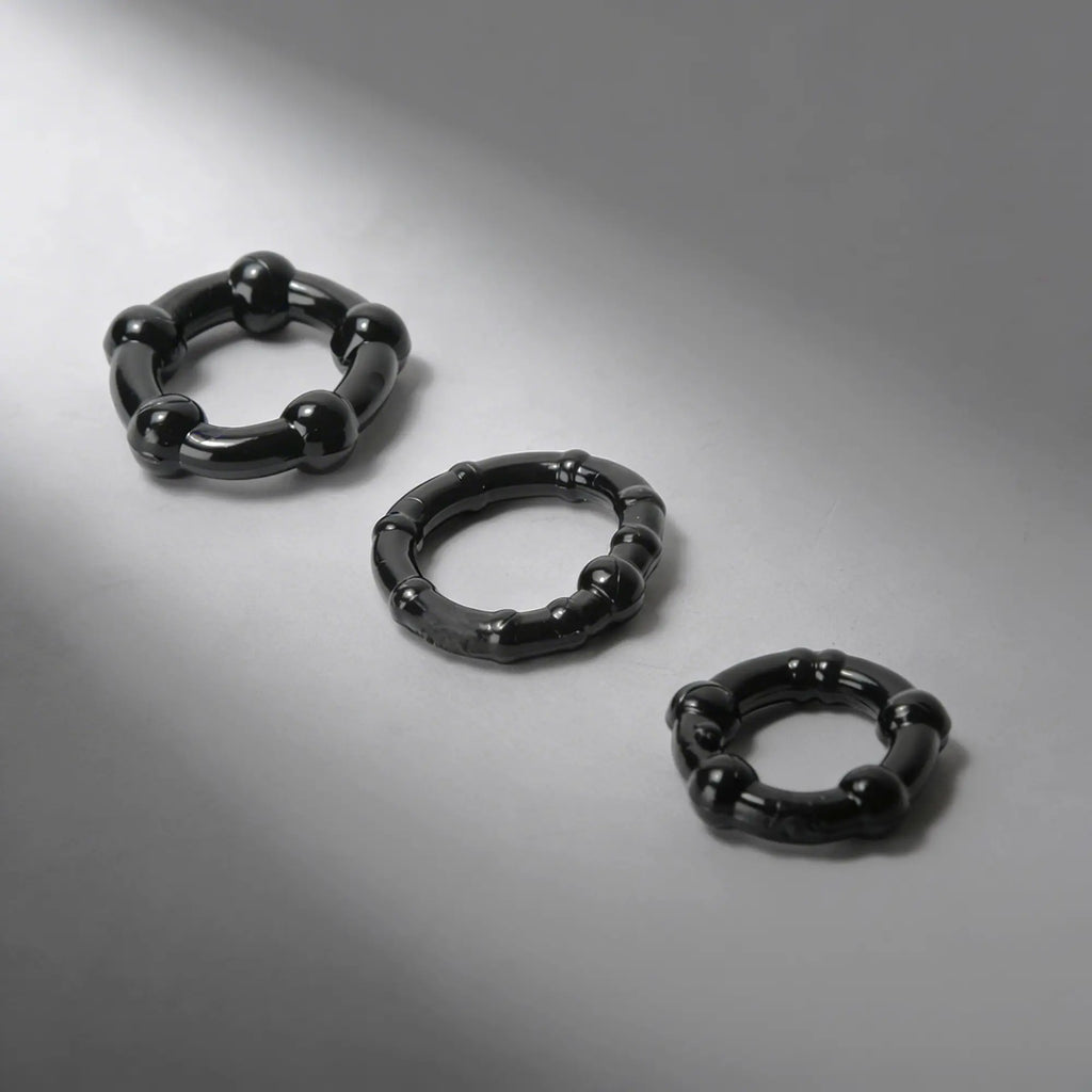 Trinity Men Erection Enhancement Rings: Three glossy black, textured silicone rings of varying sizes on a gray background.