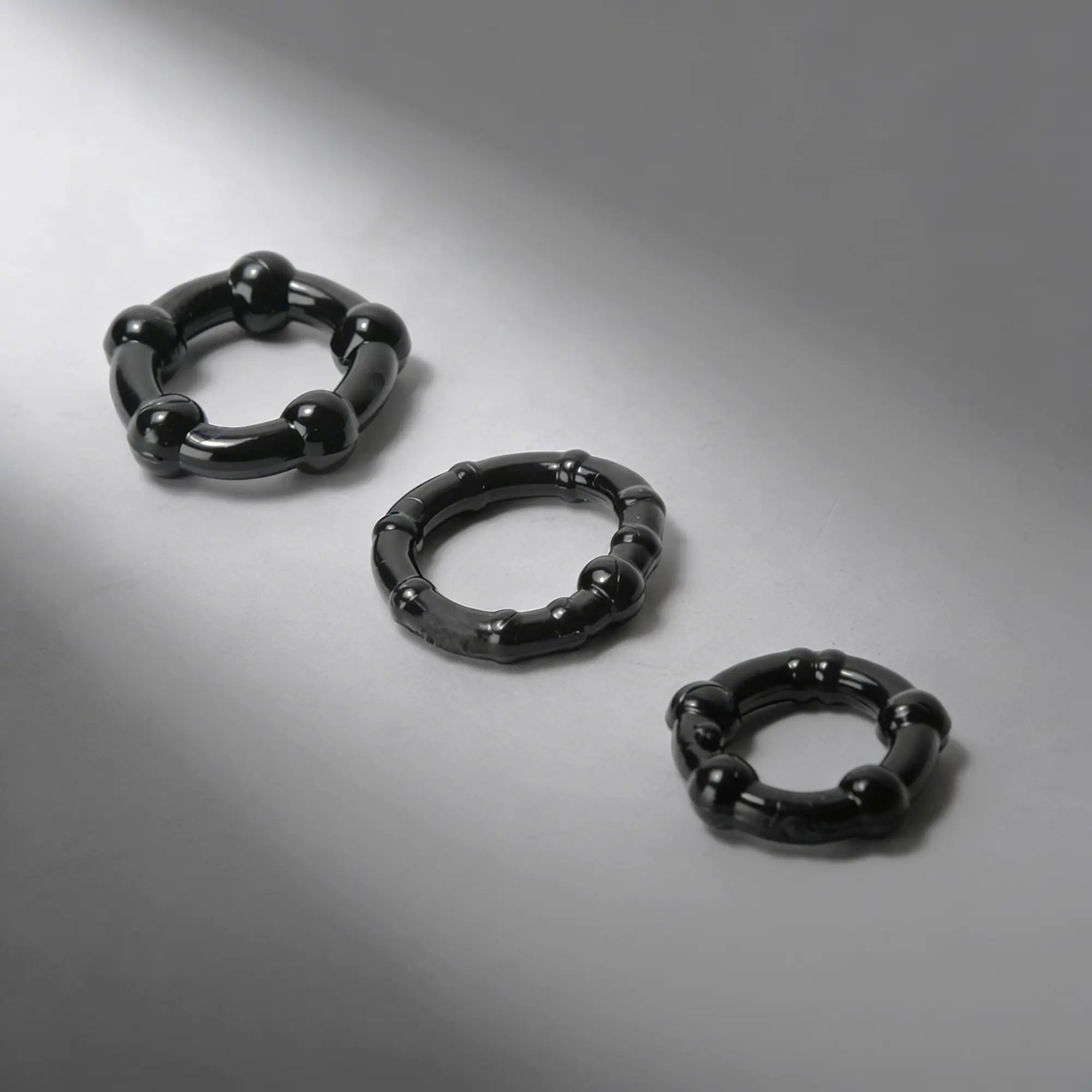 Trinity Men Erection Enhancement Rings: Three glossy black, textured silicone rings of varying sizes on a gray background.