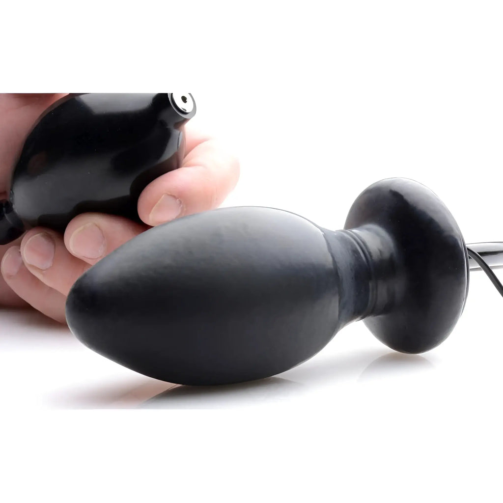 Trinity Men black inflatable, vibrating butt plug with manual pump, held in hand against a white background.