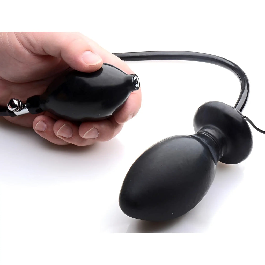 A hand holding a black Trinity inflatable butt plug with an attached pump and tube against a white background.