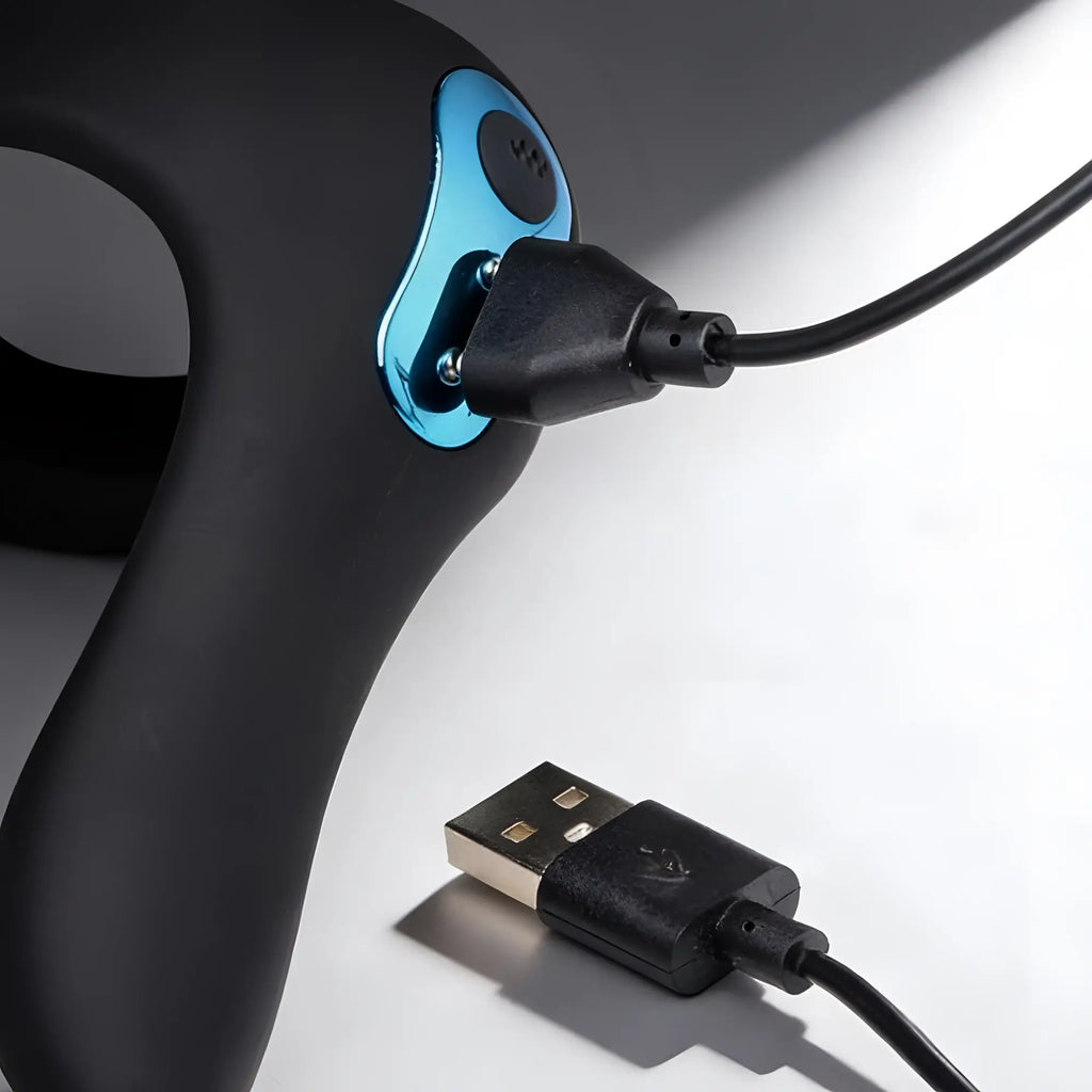 Trinity Men Power Taint 7X silicone cock and ball ring in matte black with a blue metallic charging port and USB cable.