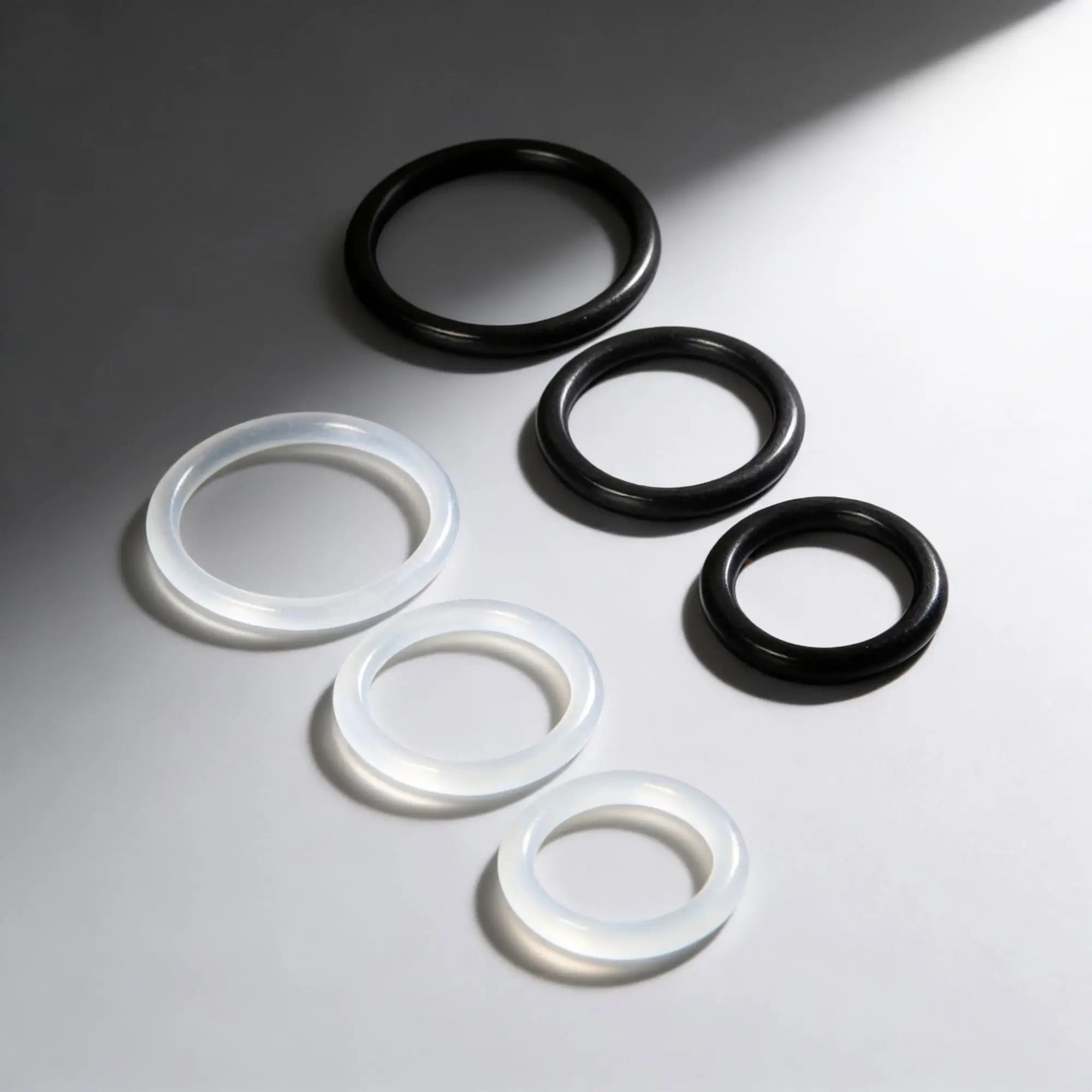Trinity Men Silicone Cock Rings: three clear and three black smooth, circular rings arranged on a white background.