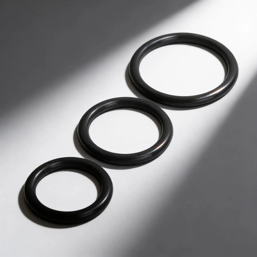 Trinity Men Silicone Cock Rings: Three smooth, black, circular rings of varying sizes arranged diagonally.