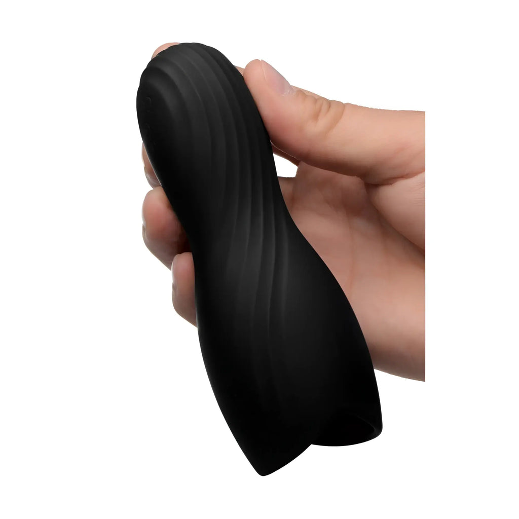 A hand holds a matte black, hourglass-shaped Trinity Men Vibrating Rechargeable Penis Pleaser with a textured finish.