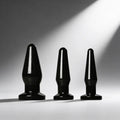 Trinity Vibes Anal Trainer Set: Three sleek, black, glossy anal plugs of varying sizes displayed against a gray background.