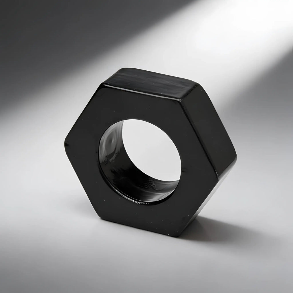 Trinity Vibes Black Hexnut cock ring, a shiny black, hexagonal-shaped ring on a neutral grey background.
