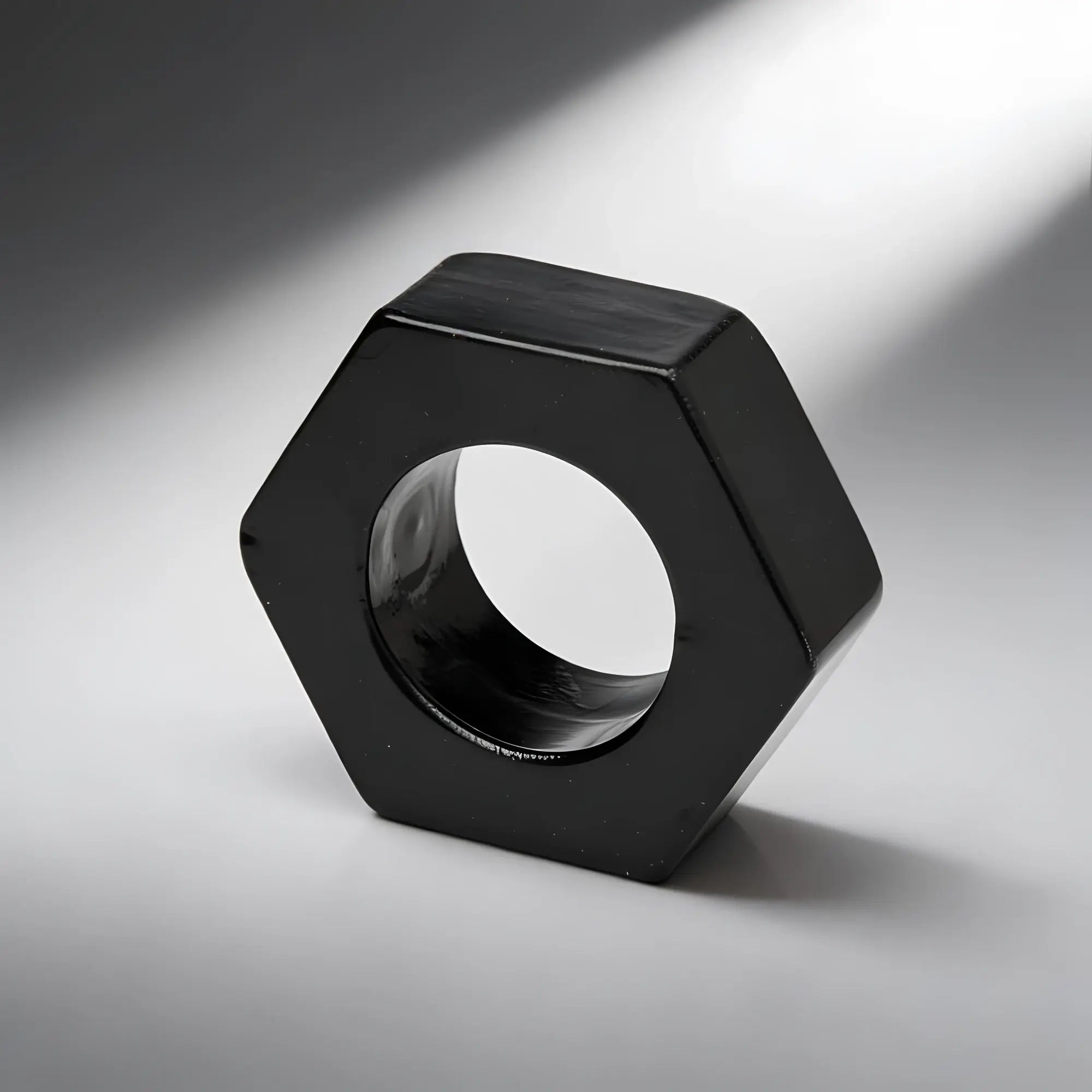 Trinity Vibes Black Hexnut cock ring, a shiny black, hexagonal-shaped ring on a neutral grey background.