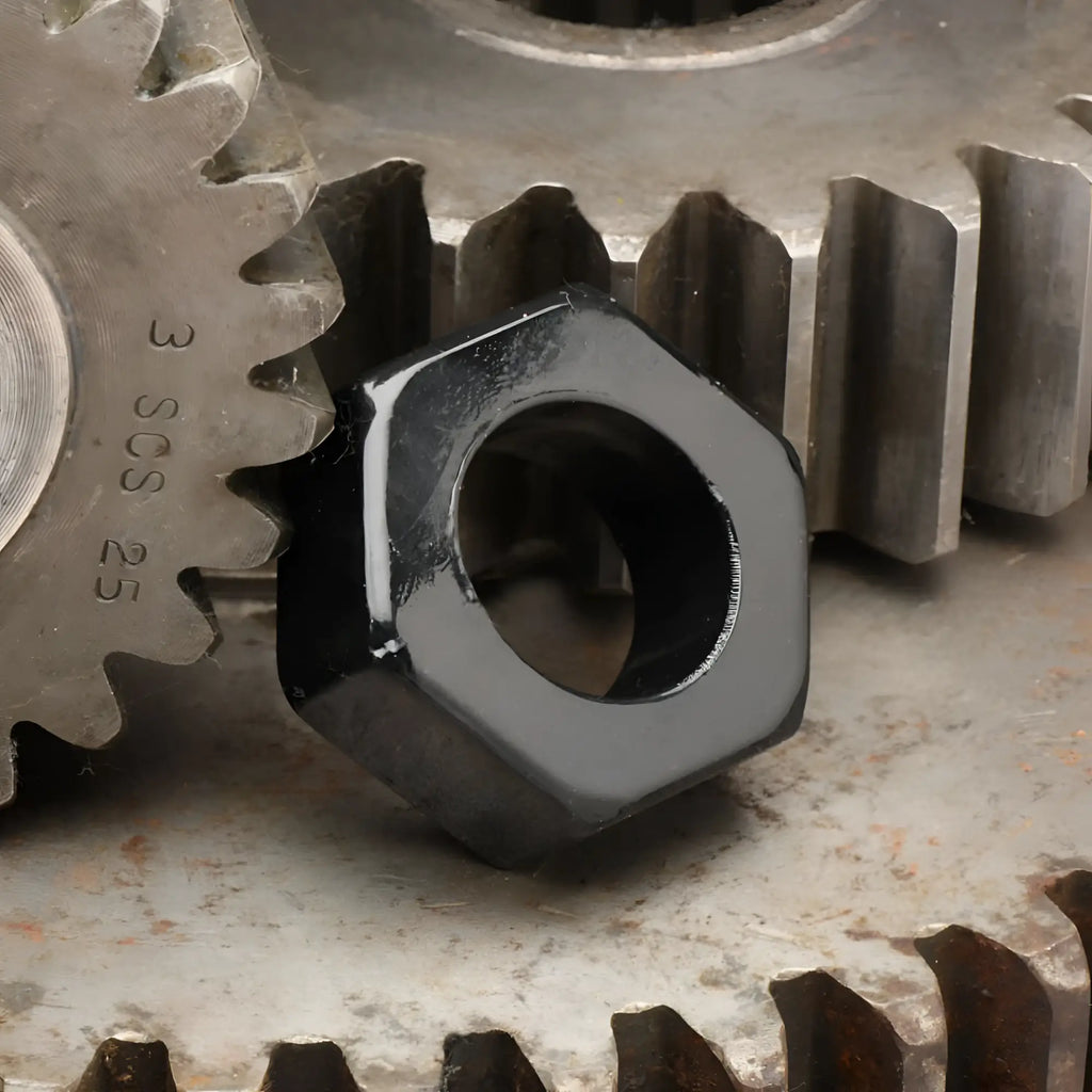 Trinity Vibes black hexnut cock ring, a shiny, hexagonal black ring resting against metallic industrial gears.