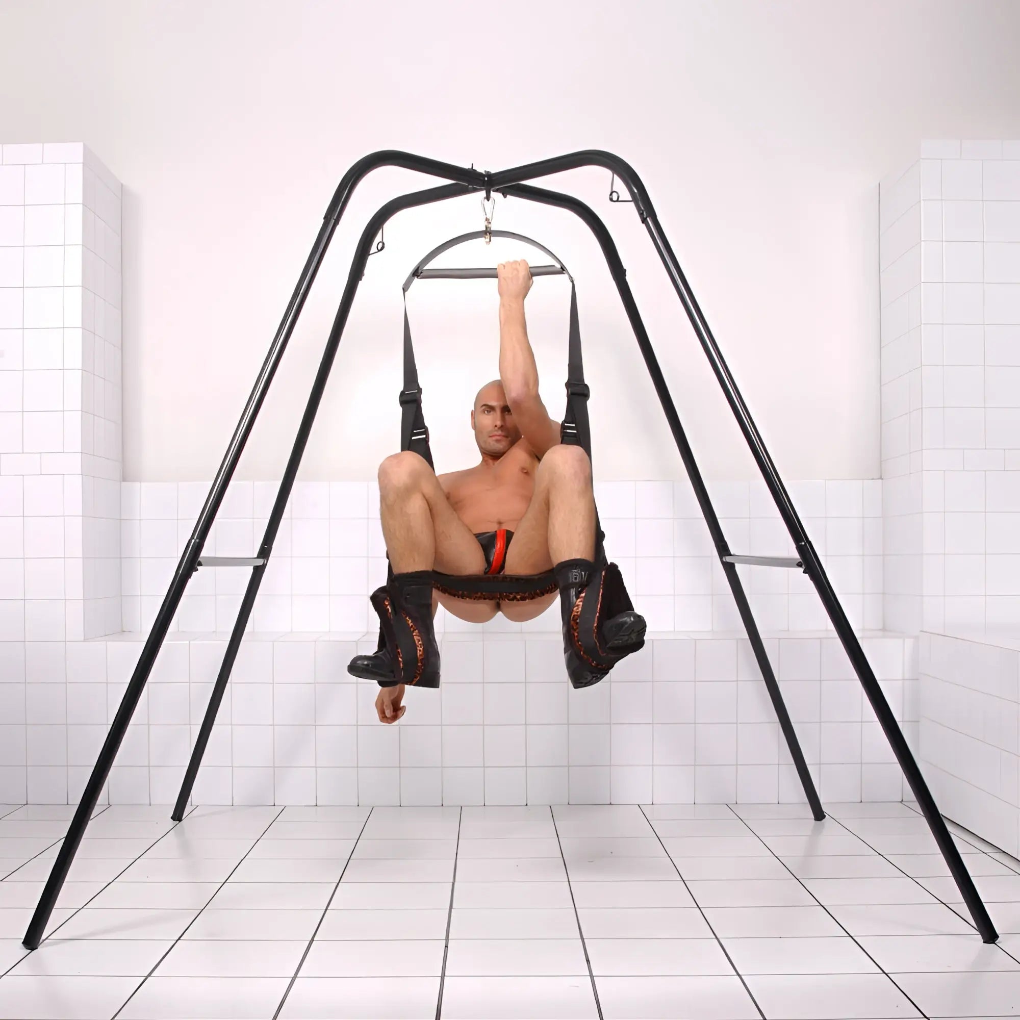 Trinity Vibes Trinity Sex Swing Stand featuring a black metal frame and an adjustable harness seat for suspension.