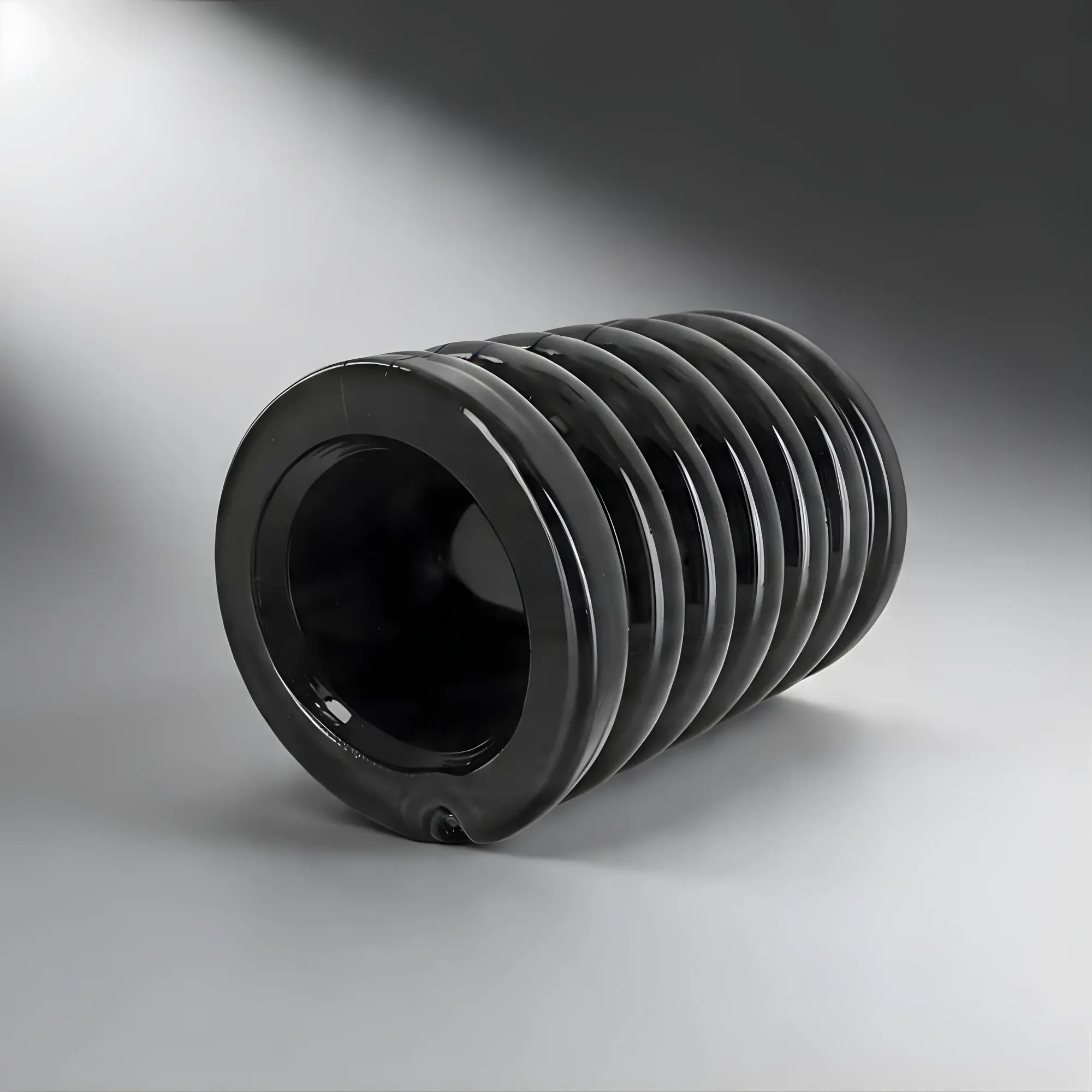Trinity Vibes Stretch-To-Fit Cock Cage: A smooth, black, cylindrical, accordion-style silicone sleeve on a gray background.