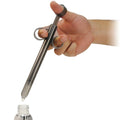A hand holds a translucent, smoky-grey Trinity Vibes XL lubricant launcher, dripping liquid into a small bottle below.