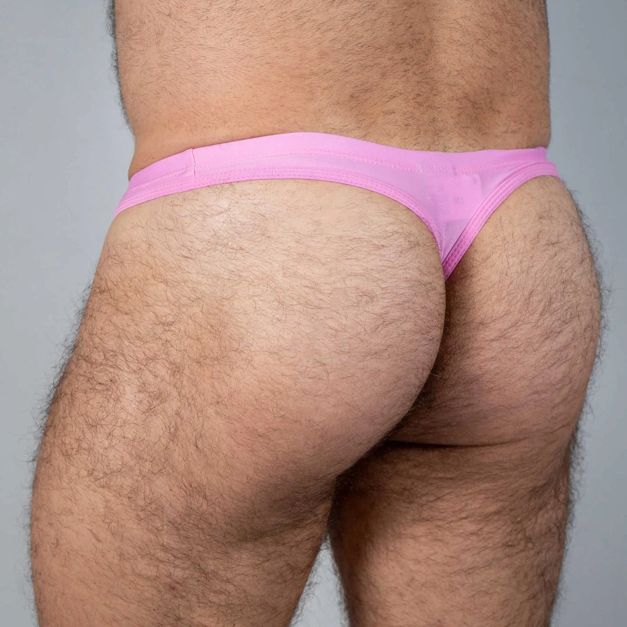 Pink tulio swim thong made of sheer fabric featuring a solid color design shown from the back side