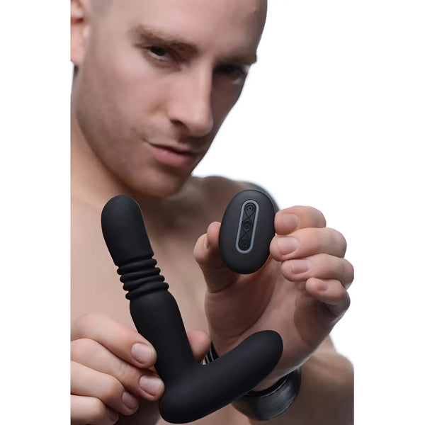 Man holding a black silicone Under Control thrusting anal plug and a matching wireless remote control.
