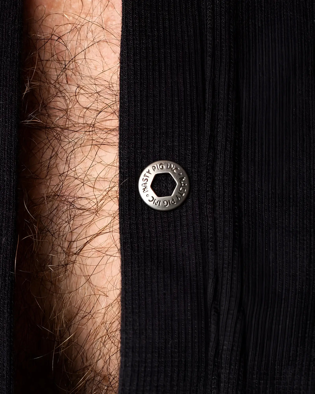 Union suit featuring a silver-toned hexagonal snap button engraved with musty pig inc on ribbed black fabric