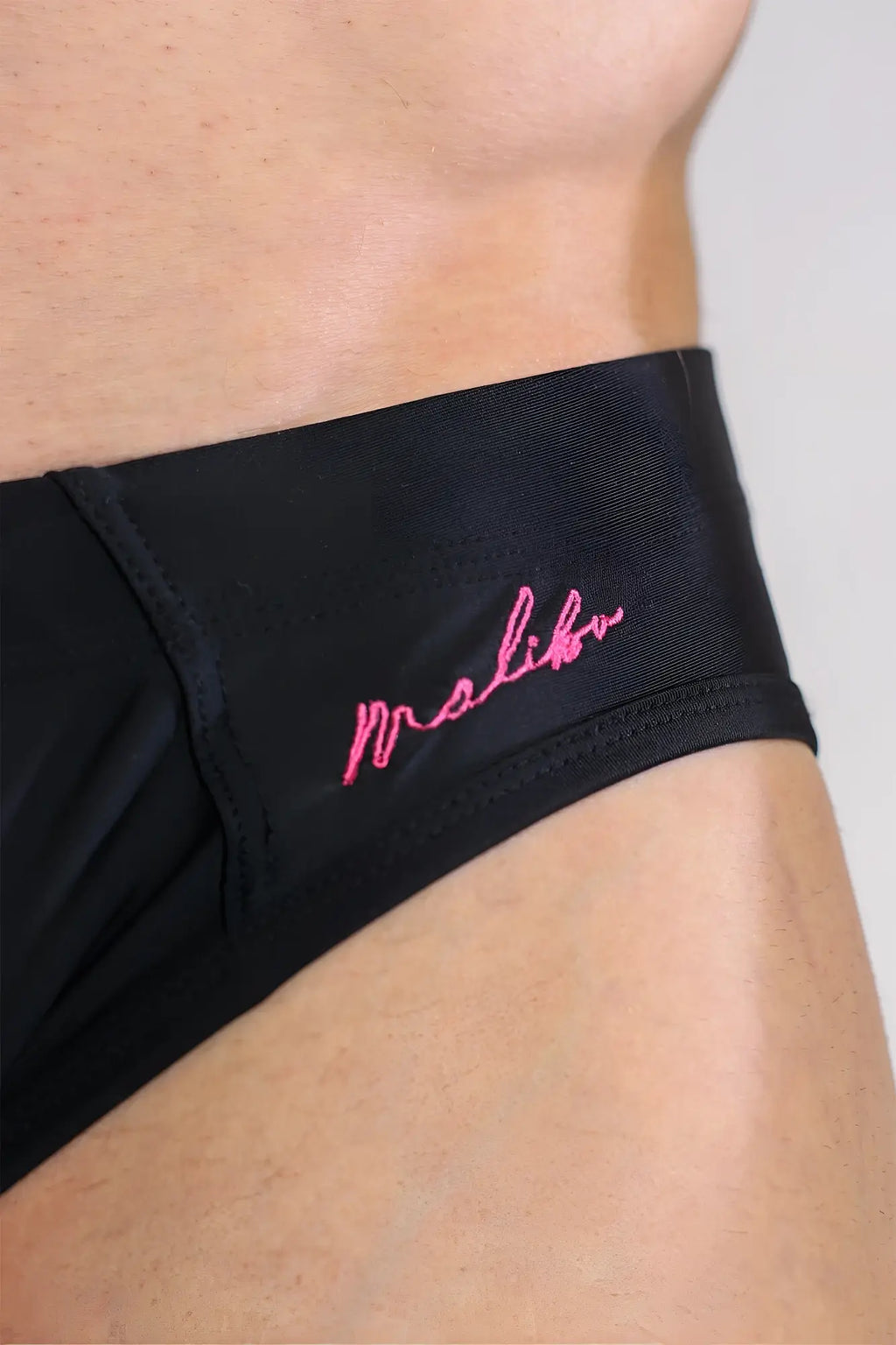 Black unzip me swim briefs featuring pink embroidered malibu branding on a sleek athletic fabric for swimming