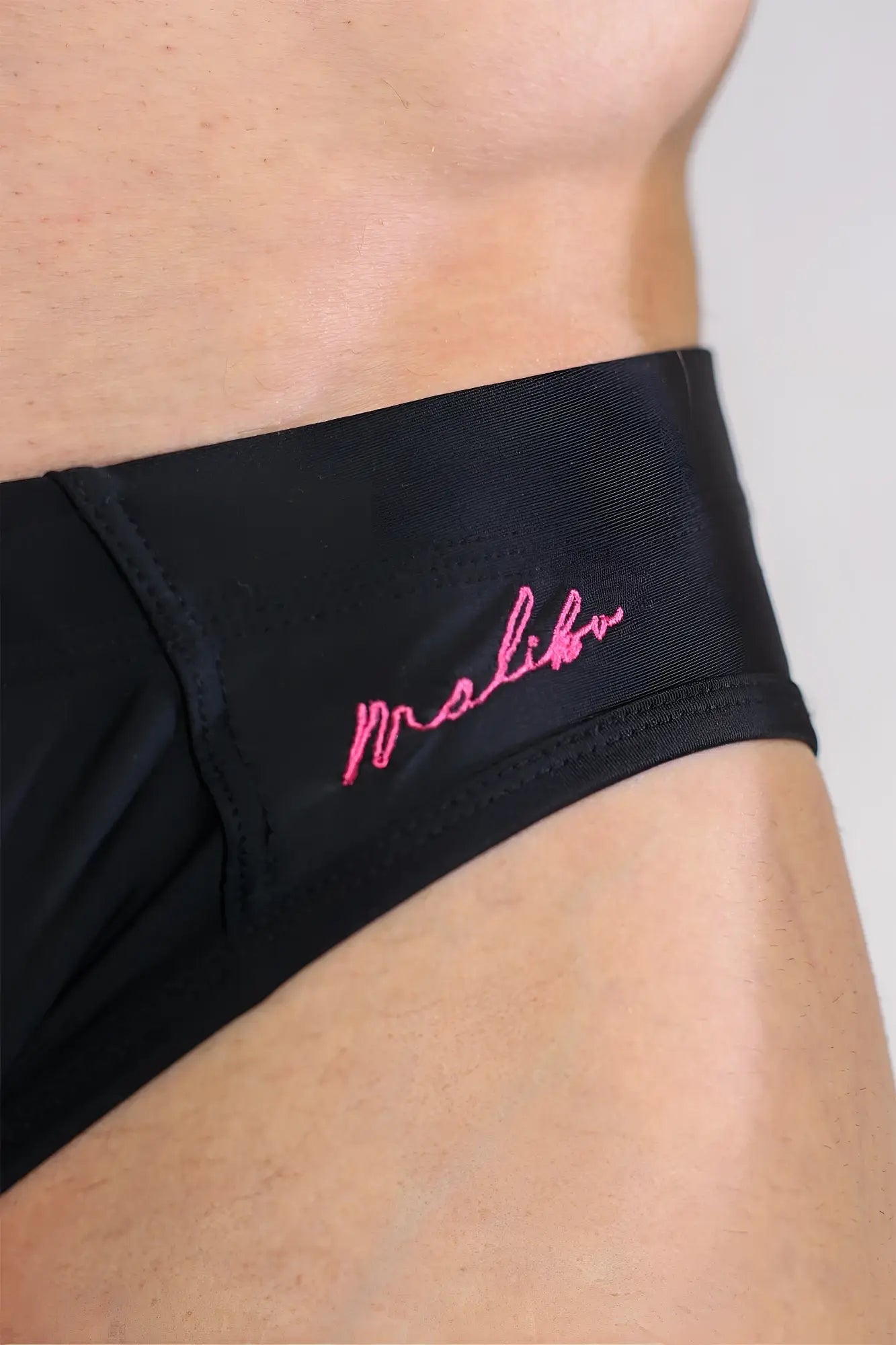 Black unzip me swim briefs featuring pink embroidered malibu branding on a sleek athletic fabric for swimming