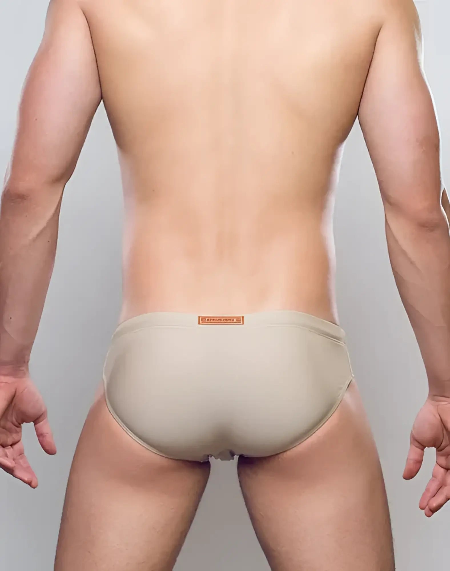 Beige form-fitting v10 core bikini swim trunks with subtle orange brand tag at the waistband