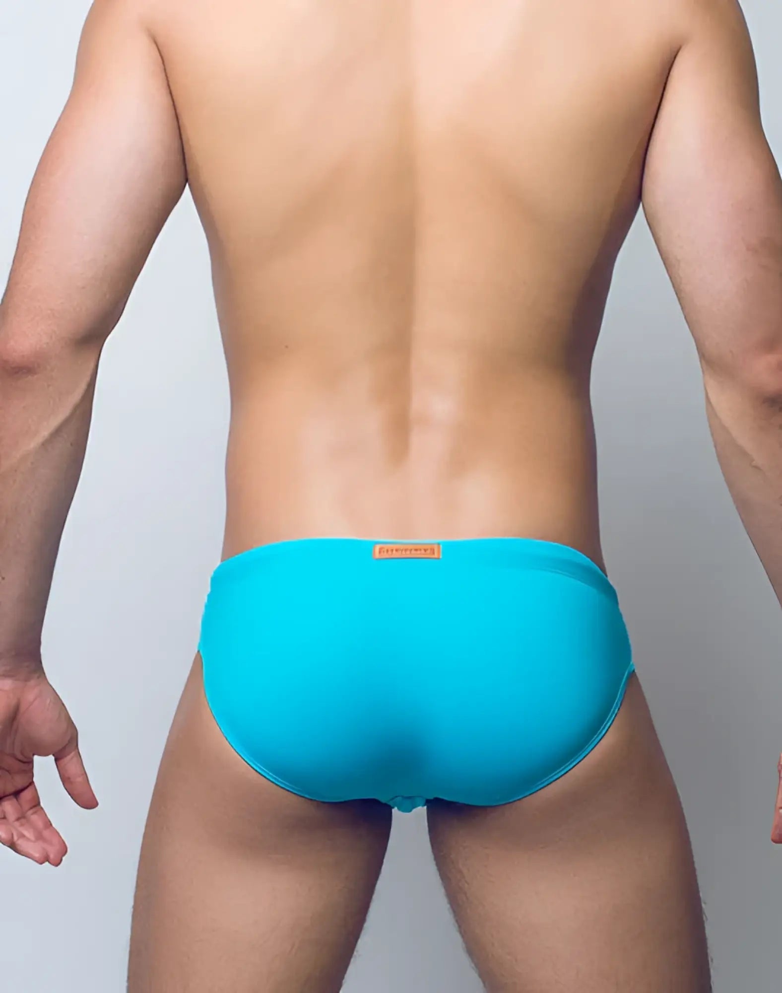 Bright turquoise V10 core bikini swim trunks with orange brand tag at the waistband for swimming and beachwear