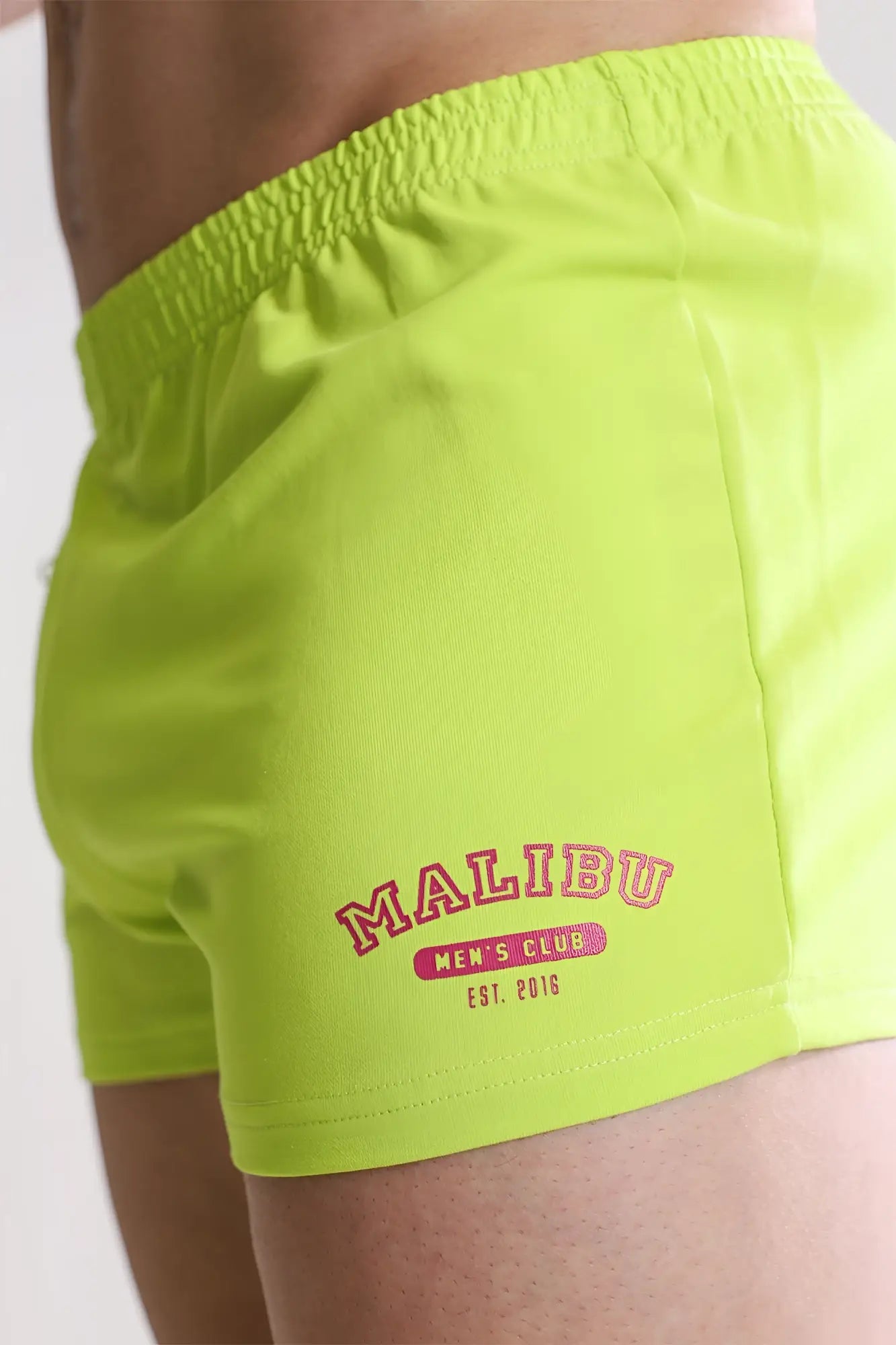 Bright neon green varsity 2 inch short shorts with red embroidered malibu men’s club and a zipper pocket