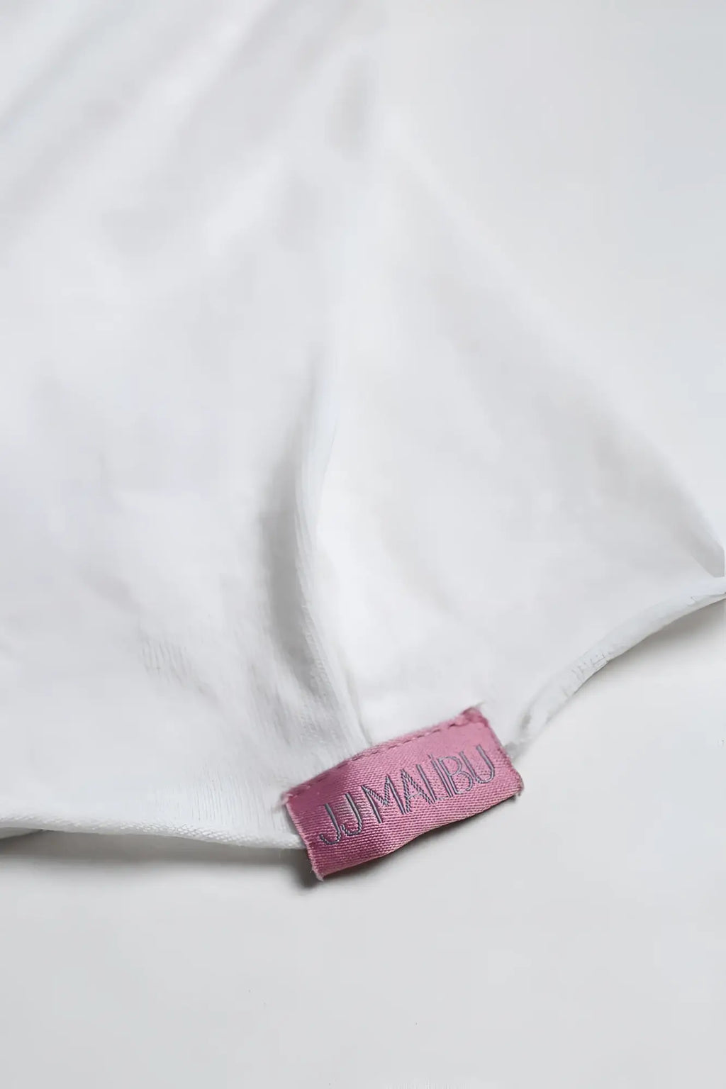 A pink satin jimau bu brand tag embroidered in darker pink sewn onto white fabric on a vintage washed drop shoulder crop tee