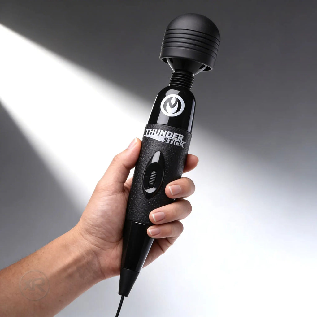 Hand holds a black Wand Essentials Thunder Stick massager with a textured grip and top control switch.
