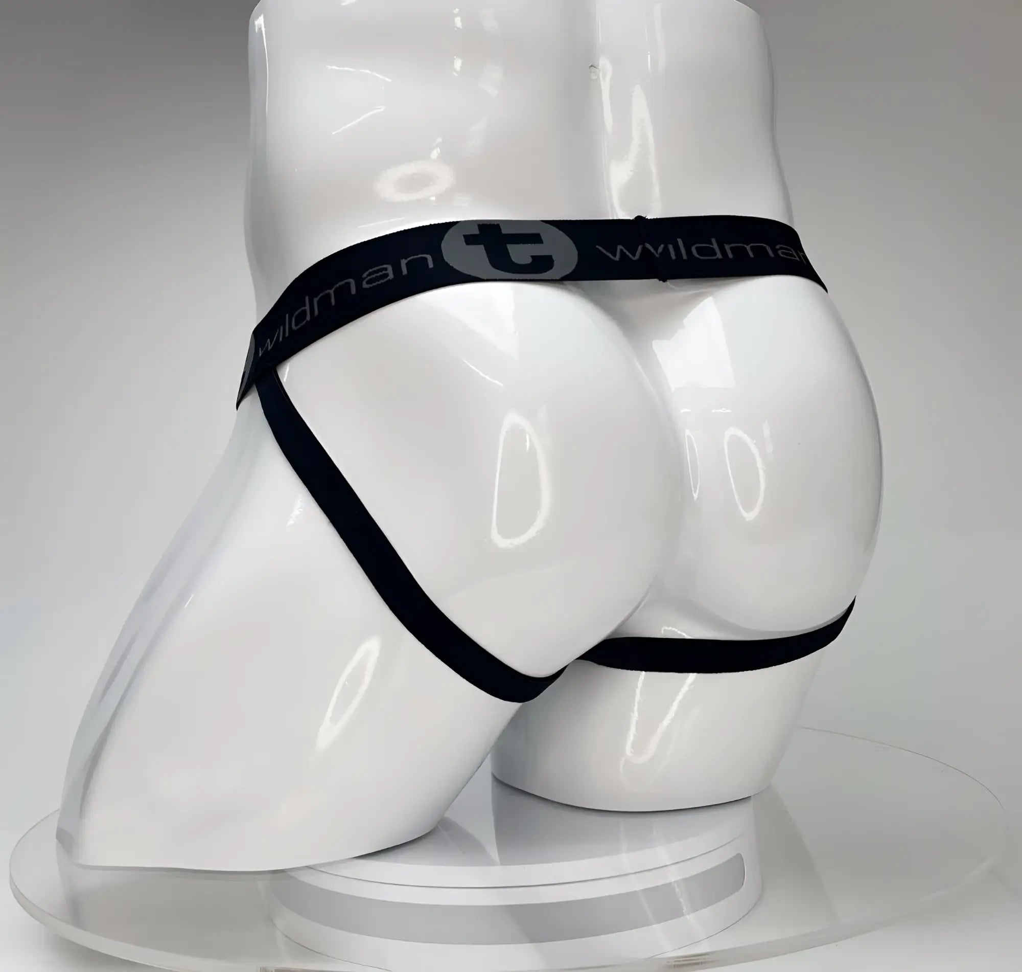 White jockstrap on a white mannequin featuring a black elastic waistband with "WildmanT" logo and leg straps.