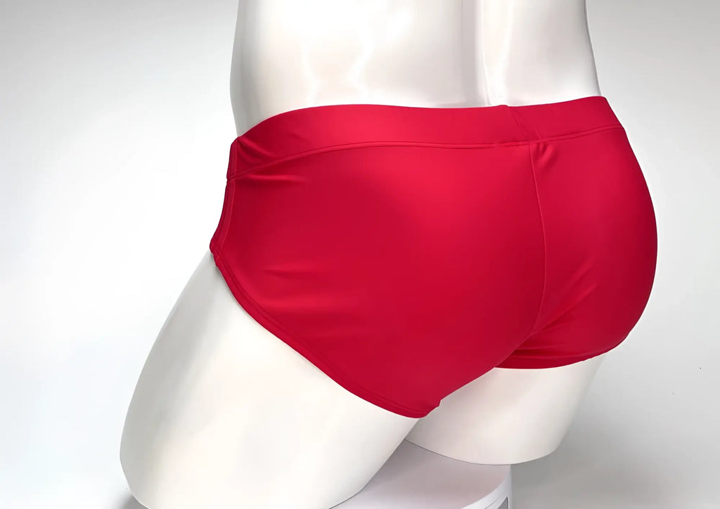Back view of WildmanT red swim brief on a white mannequin, showing a solid-colored, fitted trunk style.