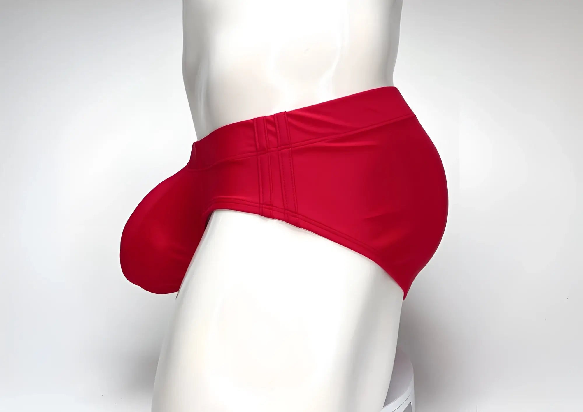 Bright red WildmanT swim brief with a prominent front pouch, shown from the side on a white mannequin torso.
