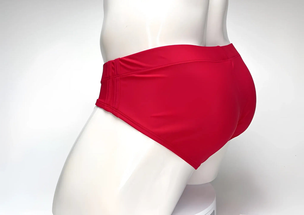 Bright red WildmanT swim brief viewed from the side on a white mannequin, featuring a wide waistband and seamless back.