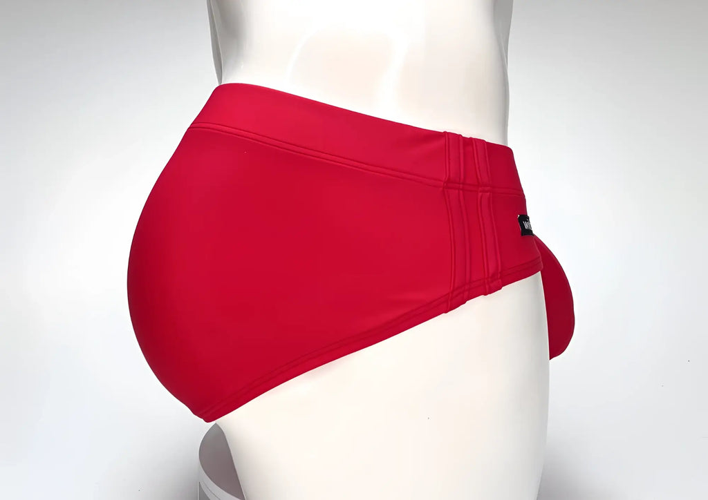 Side view of a bright red WildmanT Big Boy pouch swim brief on a white mannequin with a branded black side tag.