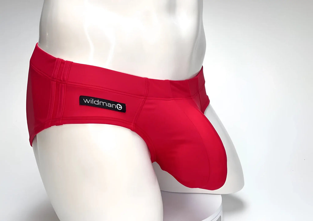 Bright red WildmanT Big Boy pouch swim brief on a white mannequin, featuring a branded black waist label.