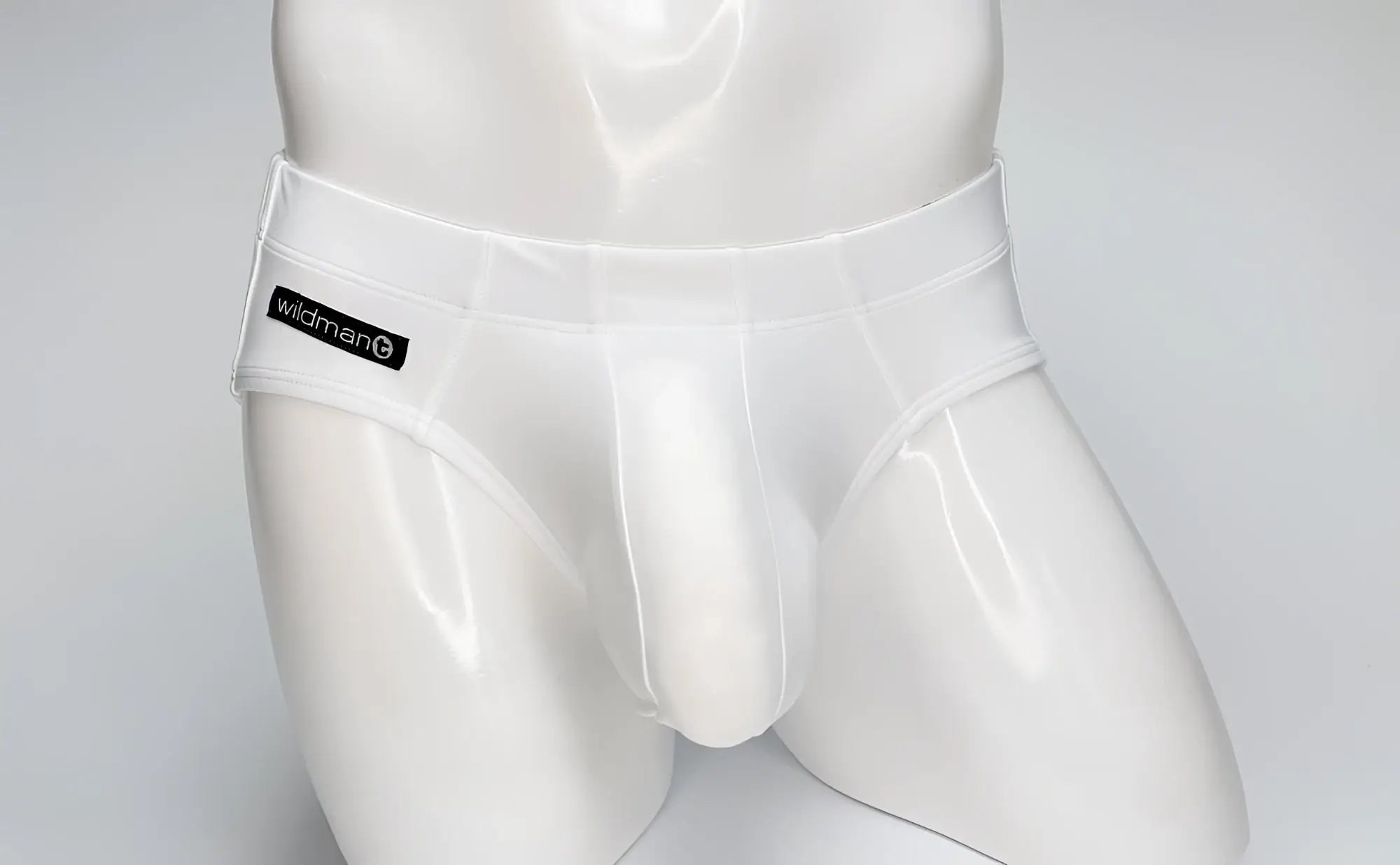 WildmanT white Big Boy pouch swim brief on a mannequin, featuring a black branded logo patch on the right hip.