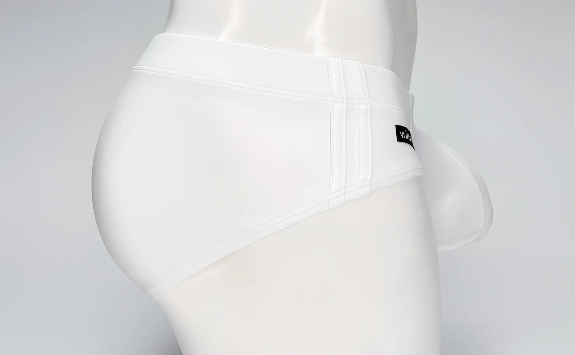 White WildmanT Big Boy pouch swim brief on a mannequin, side view showing a wide waistband and logo tag.
