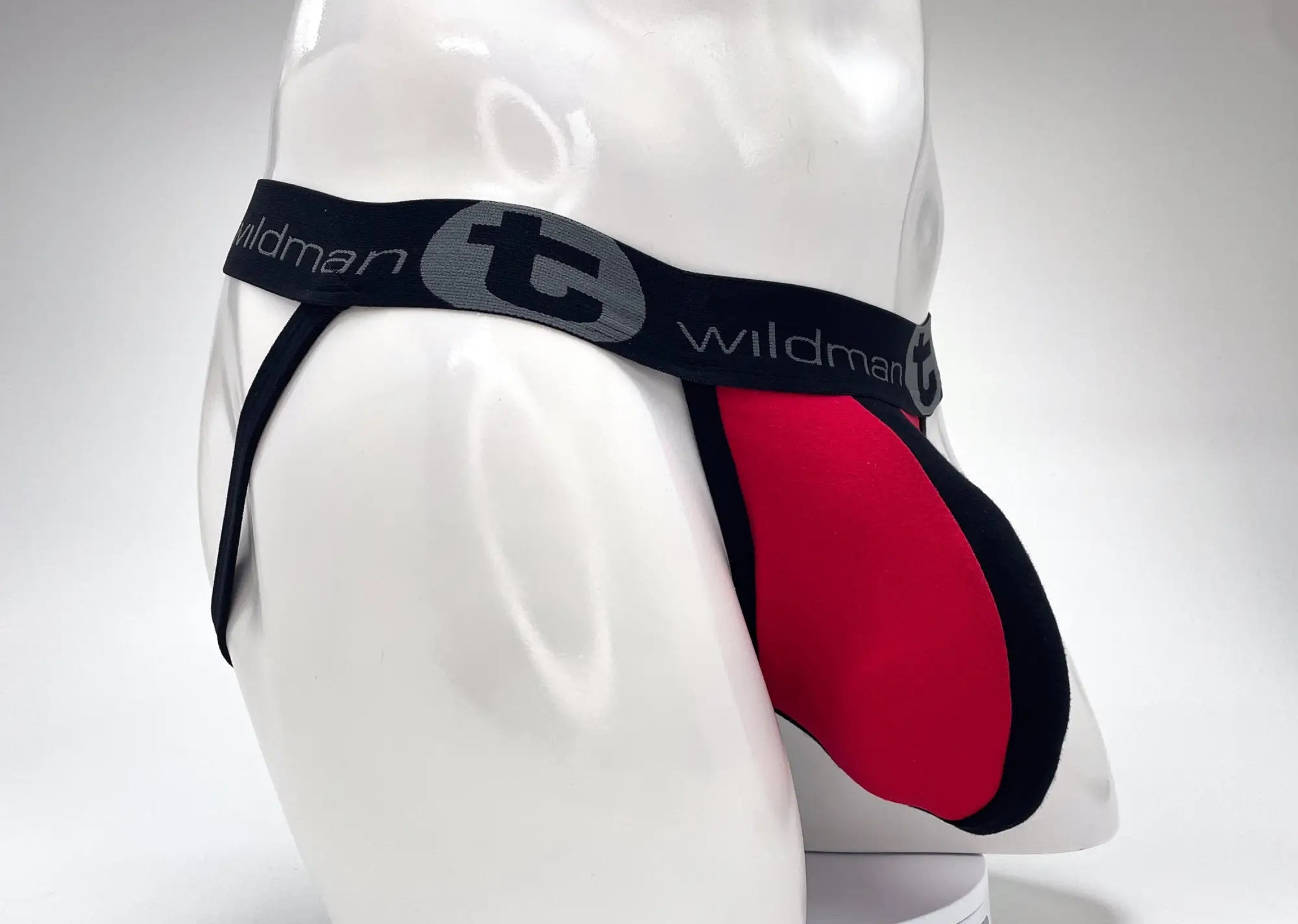 WildmanT red and black jockstrap on a mannequin, featuring a large pouch and branded elastic waistband.