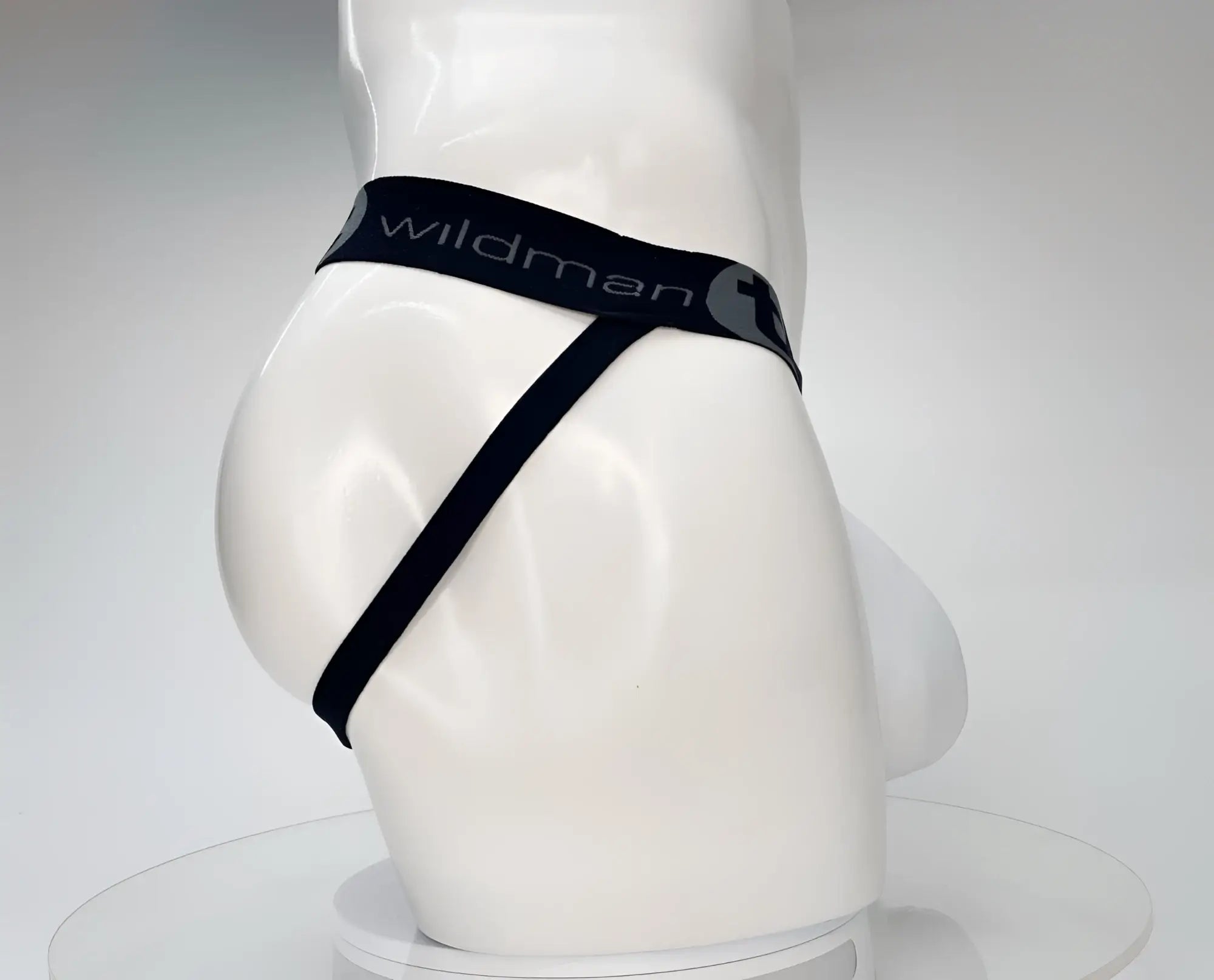 White WildmanT jockstrap on a mannequin, featuring a black waistband with gray logo text and a minimalist strap design.