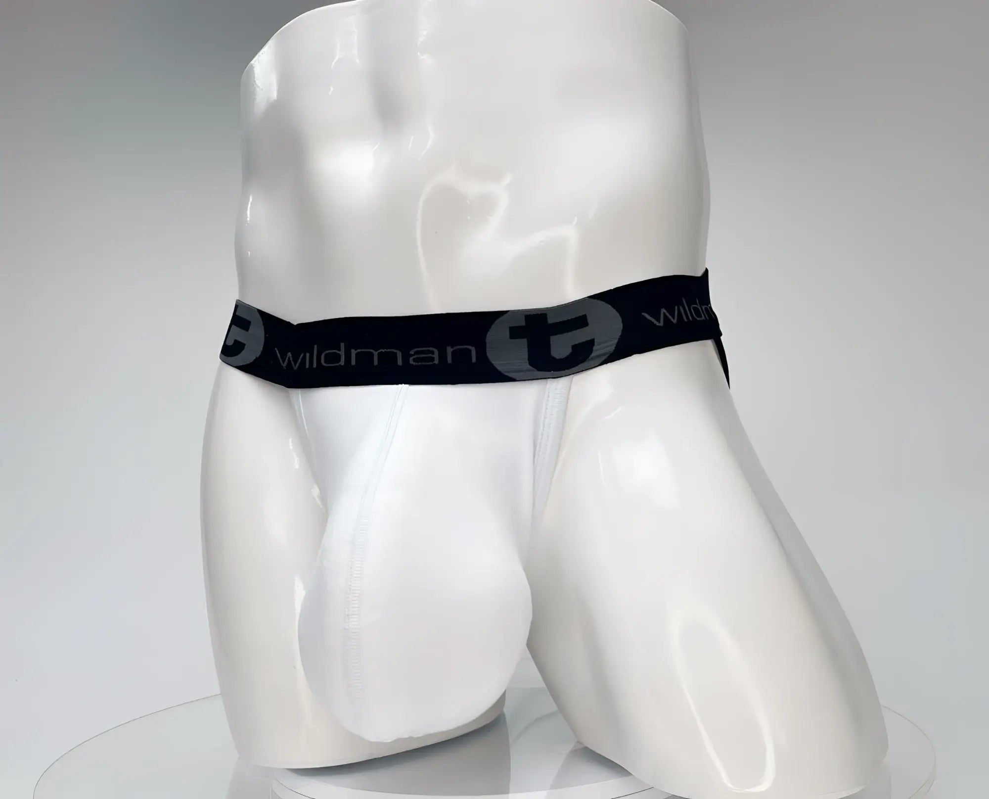 White jockstrap with a contoured pouch on a white mannequin, featuring a black waistband with "wildmanT" branding.