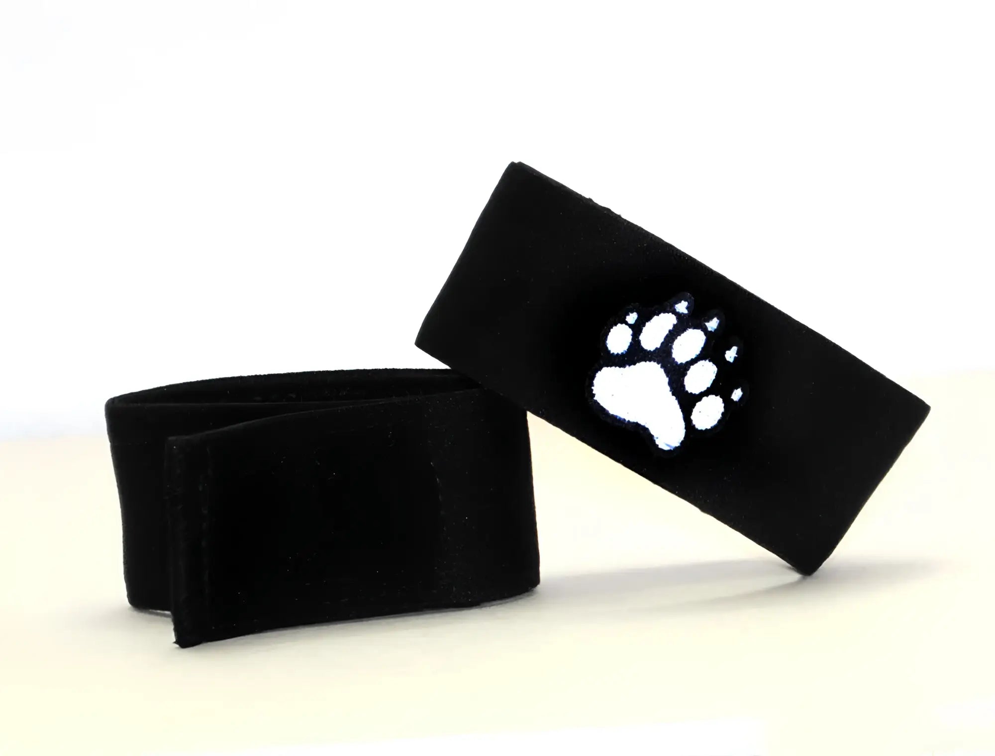 Two black adjustable fabric cock rings featuring a white embroidered bear paw print emblem.