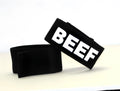 Two black fabric adjustable bands, one with "BEEF" in bold white lettering, against a plain white background.